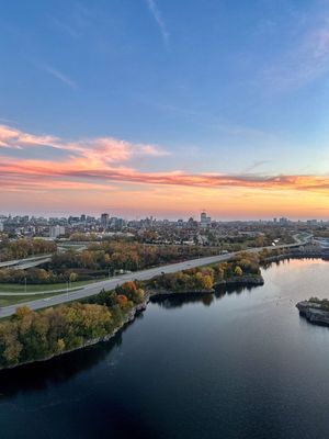 Aerial view of an urban skyline at sunset with a river bending through fall foliage and waterfront buildings.