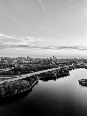 Black and white aerial cityscape view of a river winding through an urban skyline with bridges and tree-lined shores.