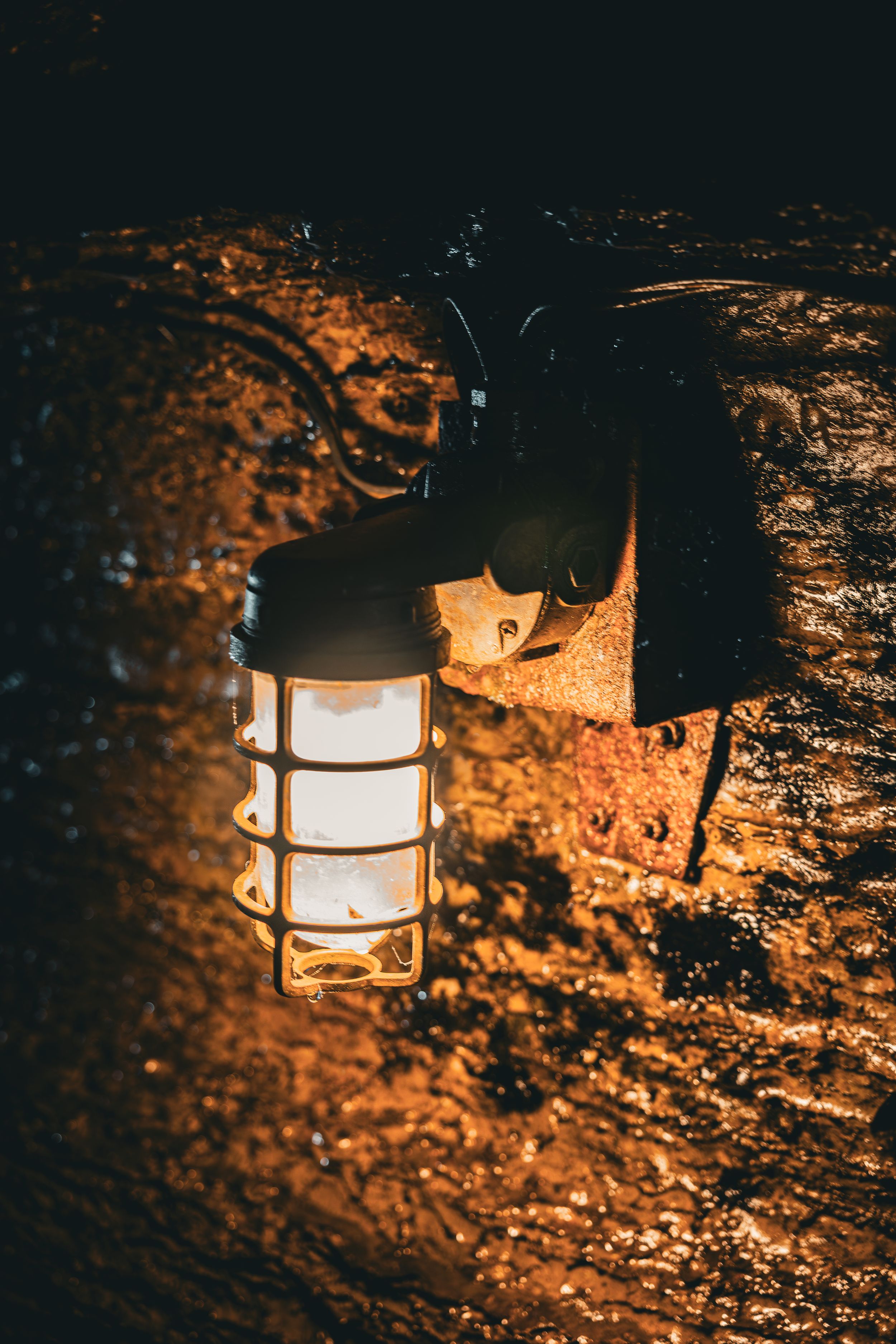 A vintage nautical-style lantern mounted on a rough stone wall glows warmly in the darkness.