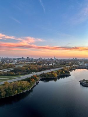 Aerial view of a city skyline at sunset with a river and autumn trees in the foreground.