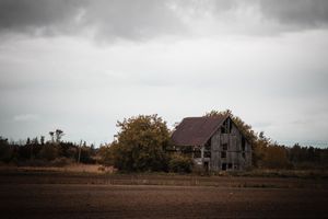 Atmospheric black and white panorama of an old farmhouse in a rural field.