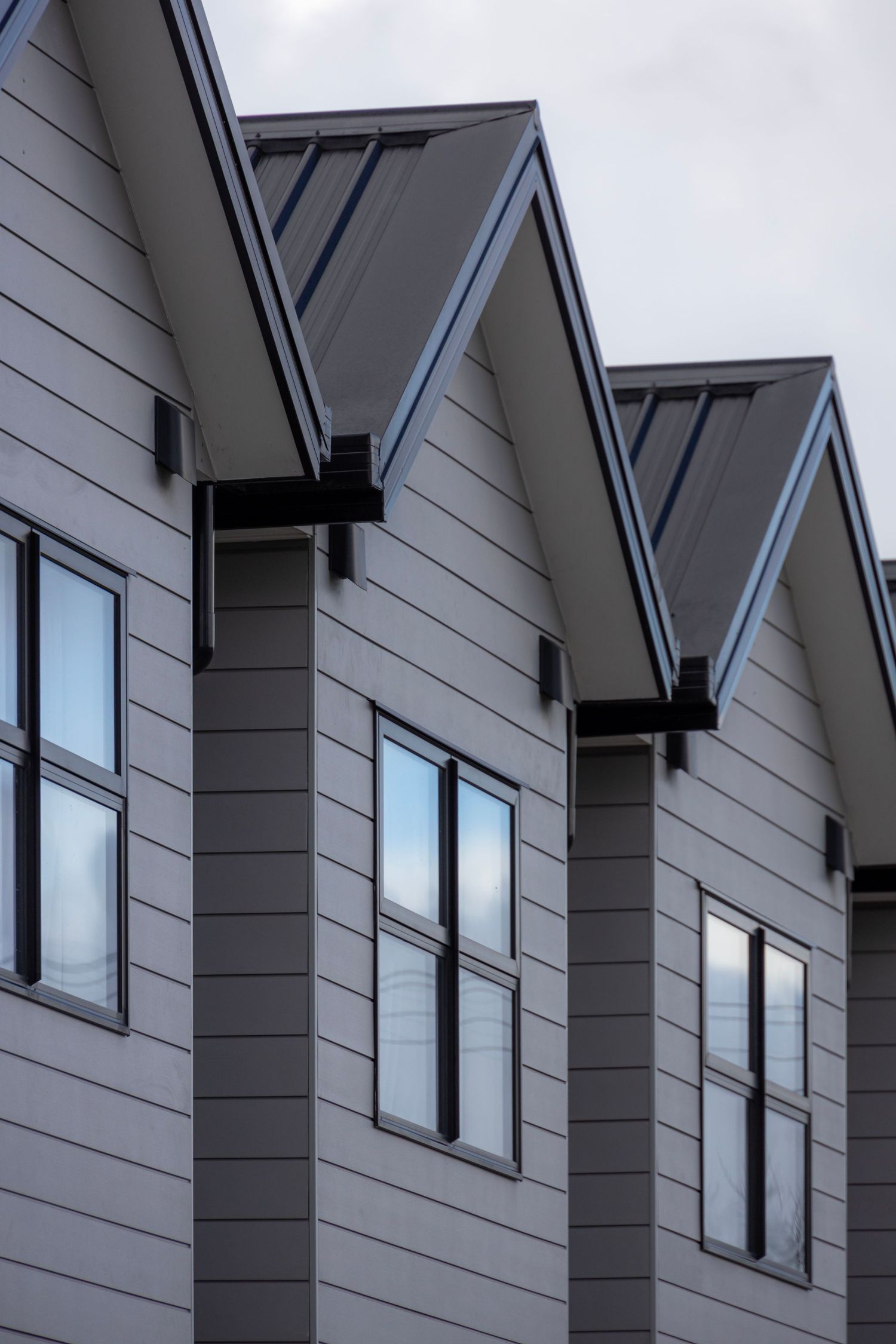 Repeating gabled roofline on grey townhouses, each facade catching subtle dusk light.