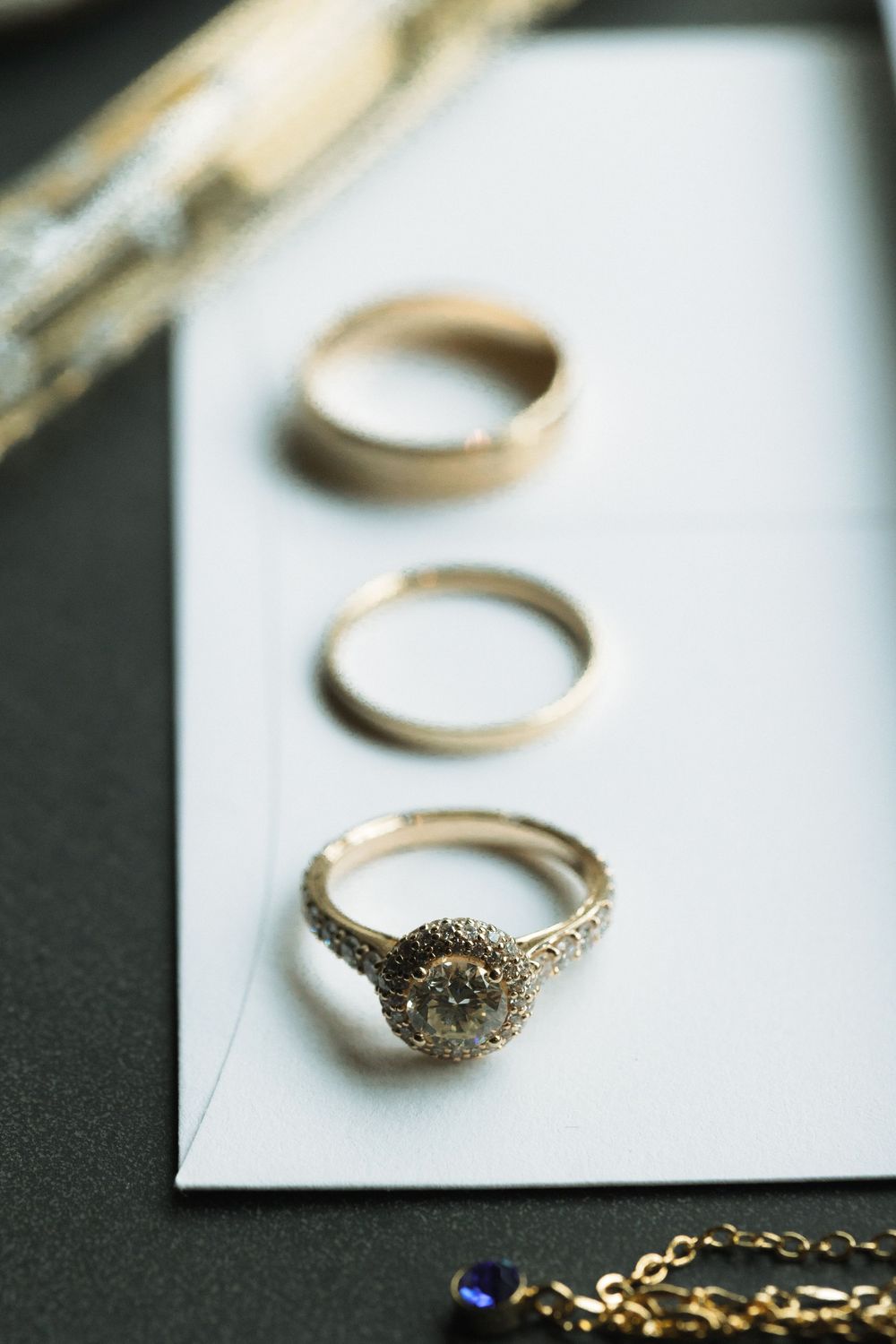 Three elegant rings arranged in a row on white surface, with a glamorous diamond engagement ring at the bottom.