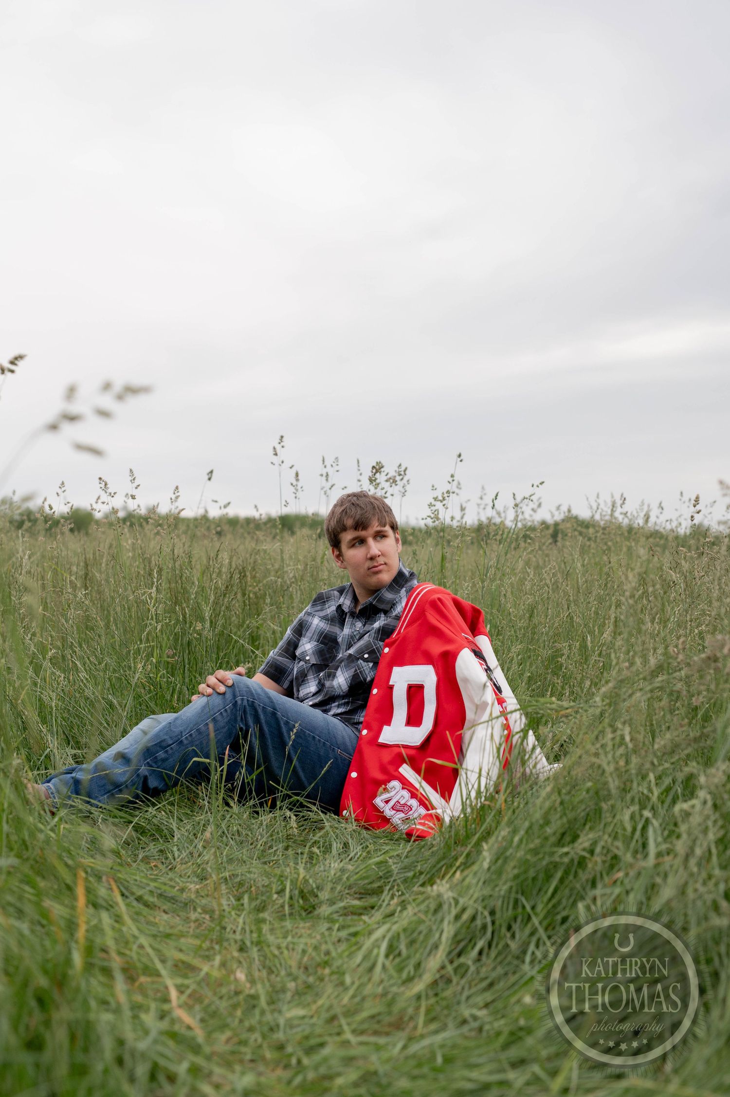 A person in a red jersey and plaid shirt lies in a grass field against an overcast sky.