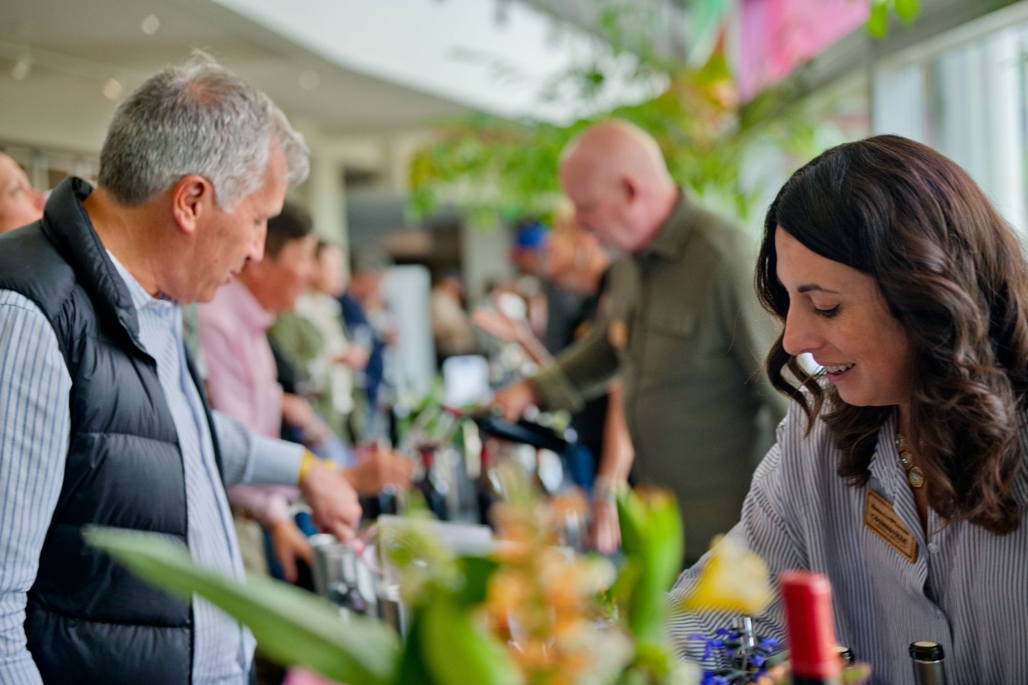 Customers browse and interact at a bustling indoor marketplace with decorative plants and vendor displays.