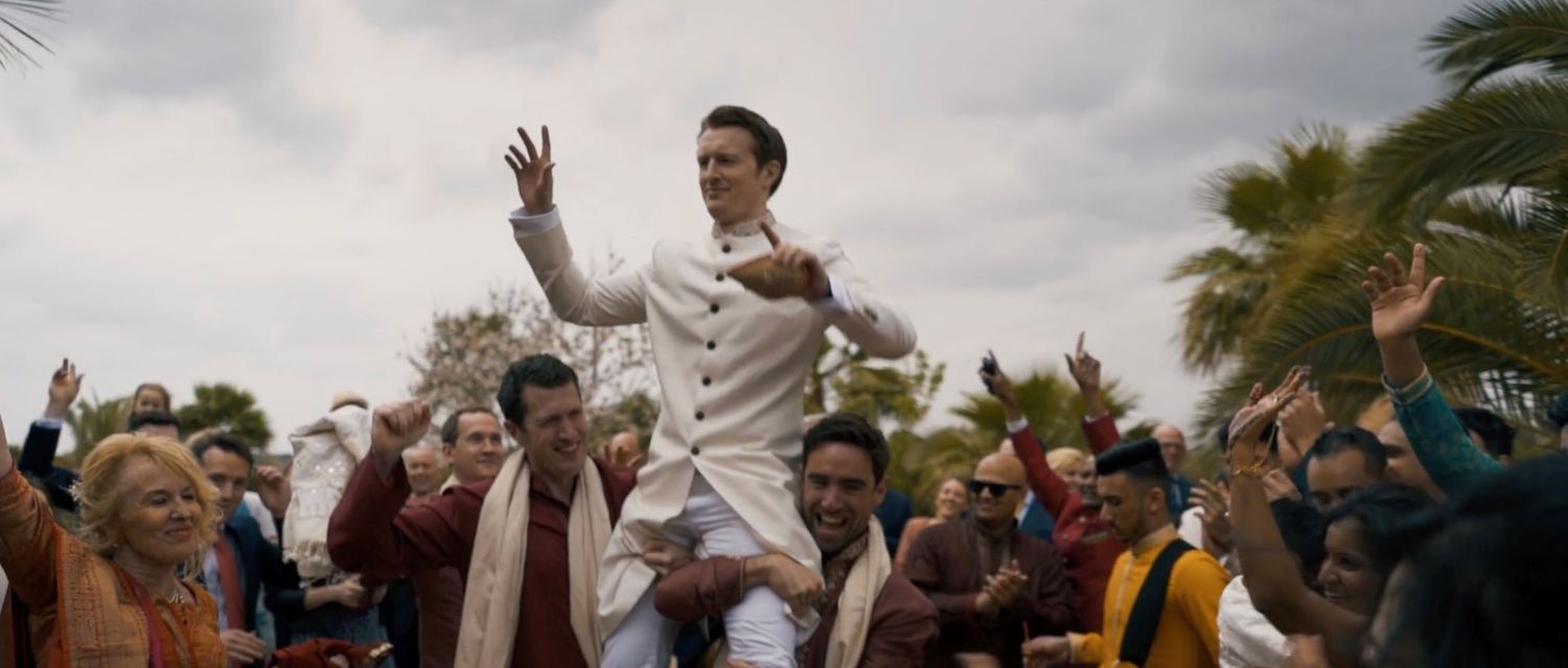 Groom dressed in white being lifted by his friends in a joyful outdoor celebration with dancing.