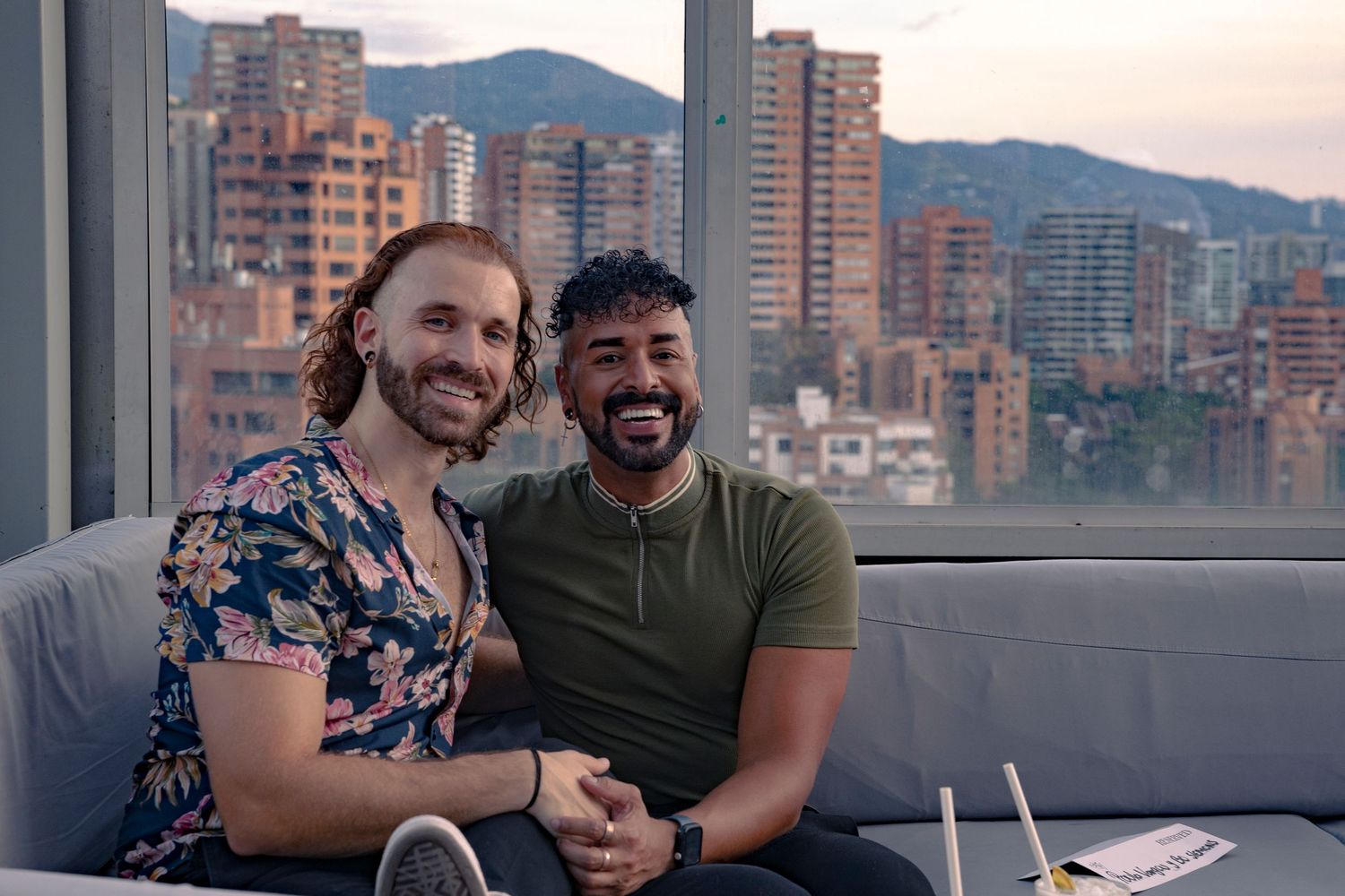 A couple pose for a portrait enjoying an evening on an outdoor patio with city buildings and mountains in the background at sunset.