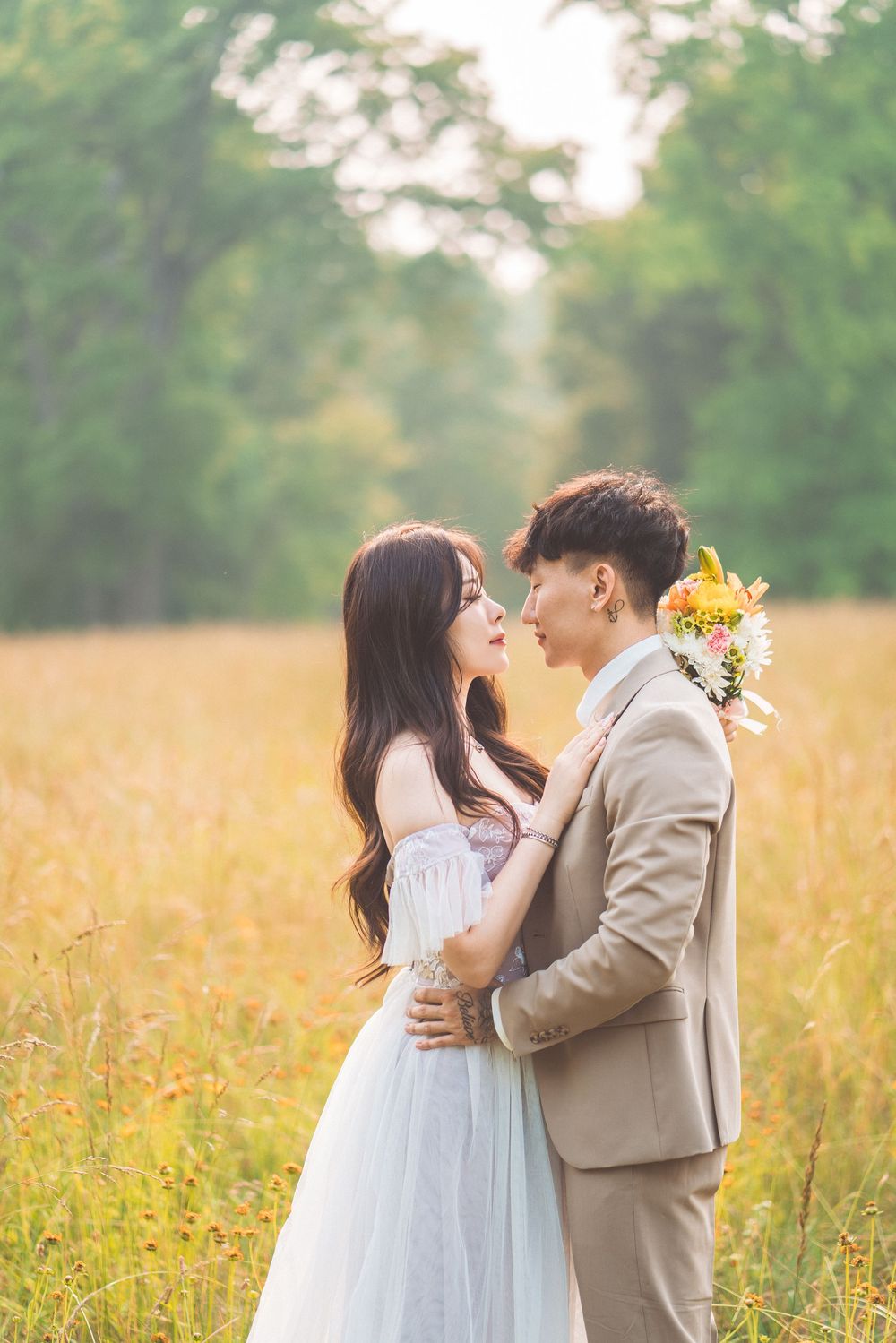 Couple in formal wear sharing intimate moment in golden wheat field at sunset.