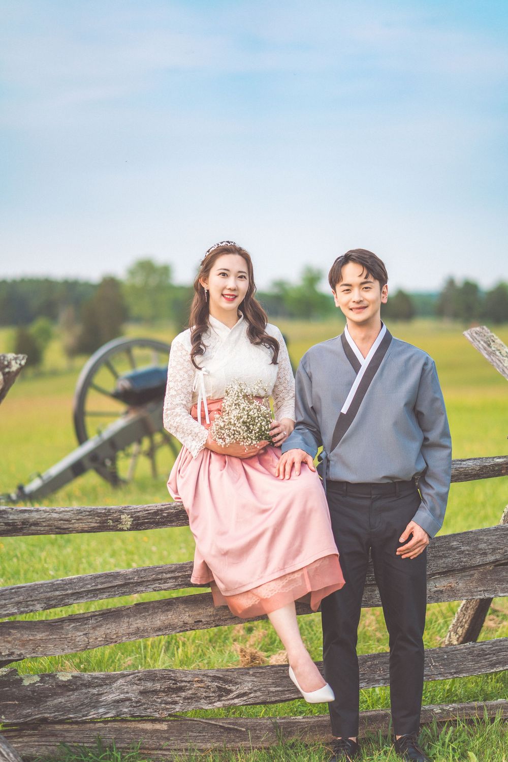 Couple in romantic photoshoot pose by rustic fence with vintage cannon in background.