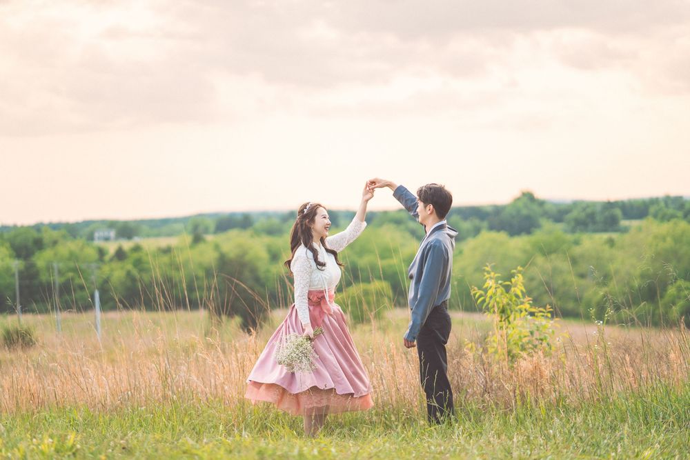 Couple dancing together in flowing pink dress and grey suit in summer meadow.