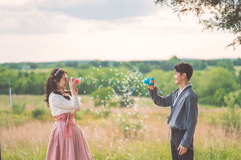 Playful couple blowing flower petals at each other in sunny meadow.