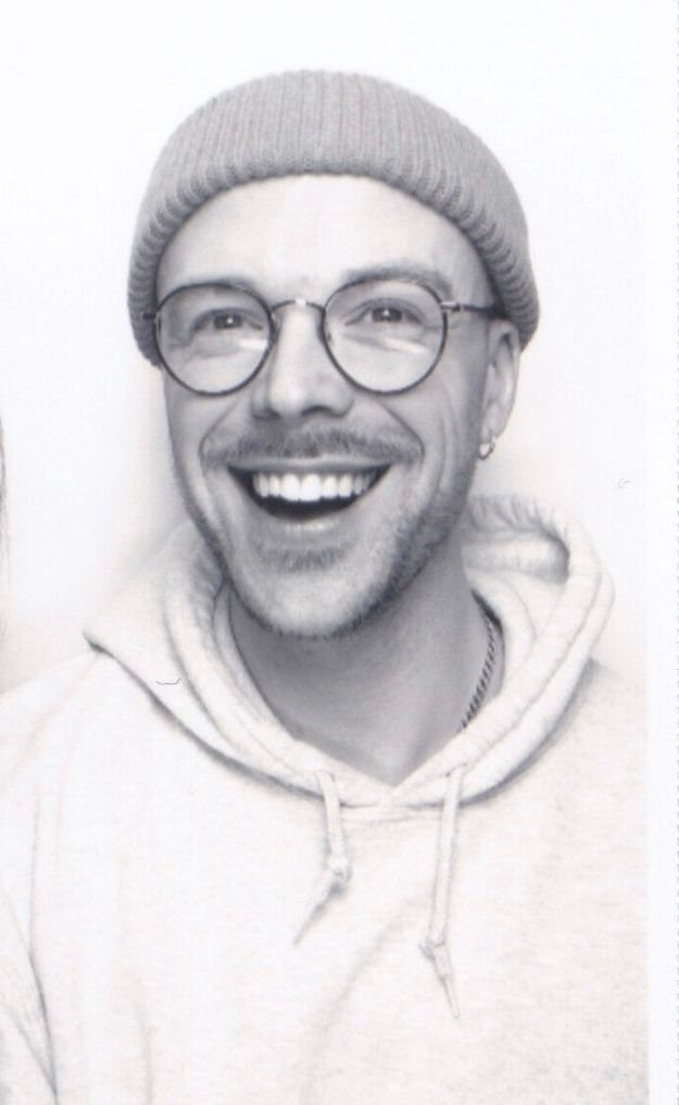 Black and white portrait of person wearing glasses and gray beanie with bright smile.