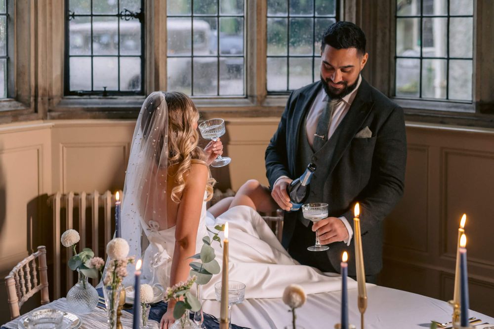 Wedding couple pouring champagne together at an intimate reception table with lit candles.