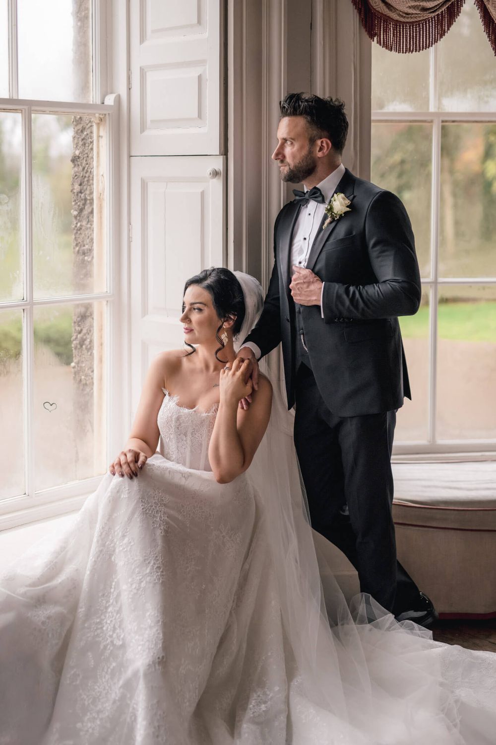 Elegant wedding portrait by bright window with couple in formal attire.