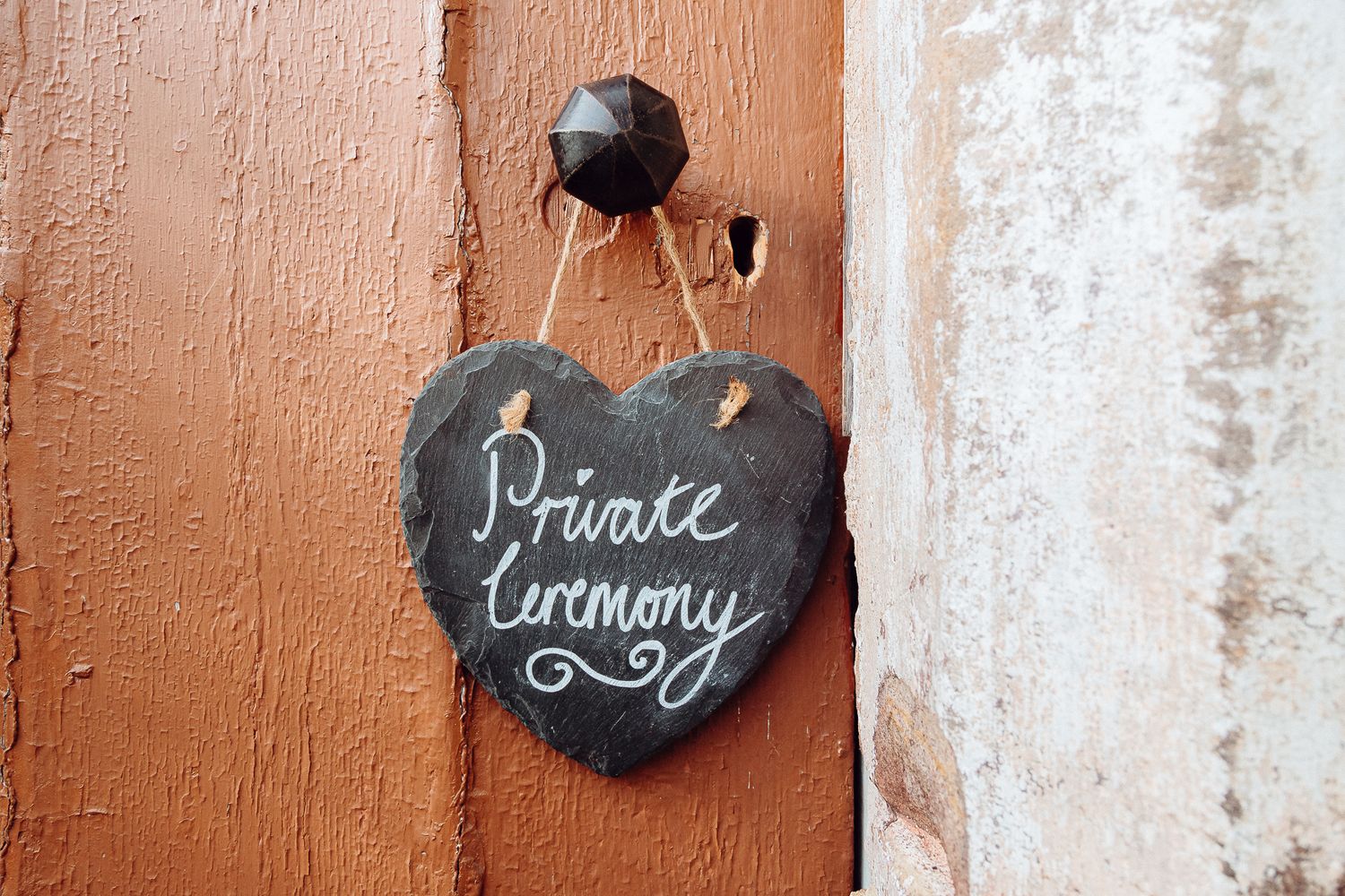 A heart-shaped slate sign reading 'Private ceremony' hangs on a brown wooden door.