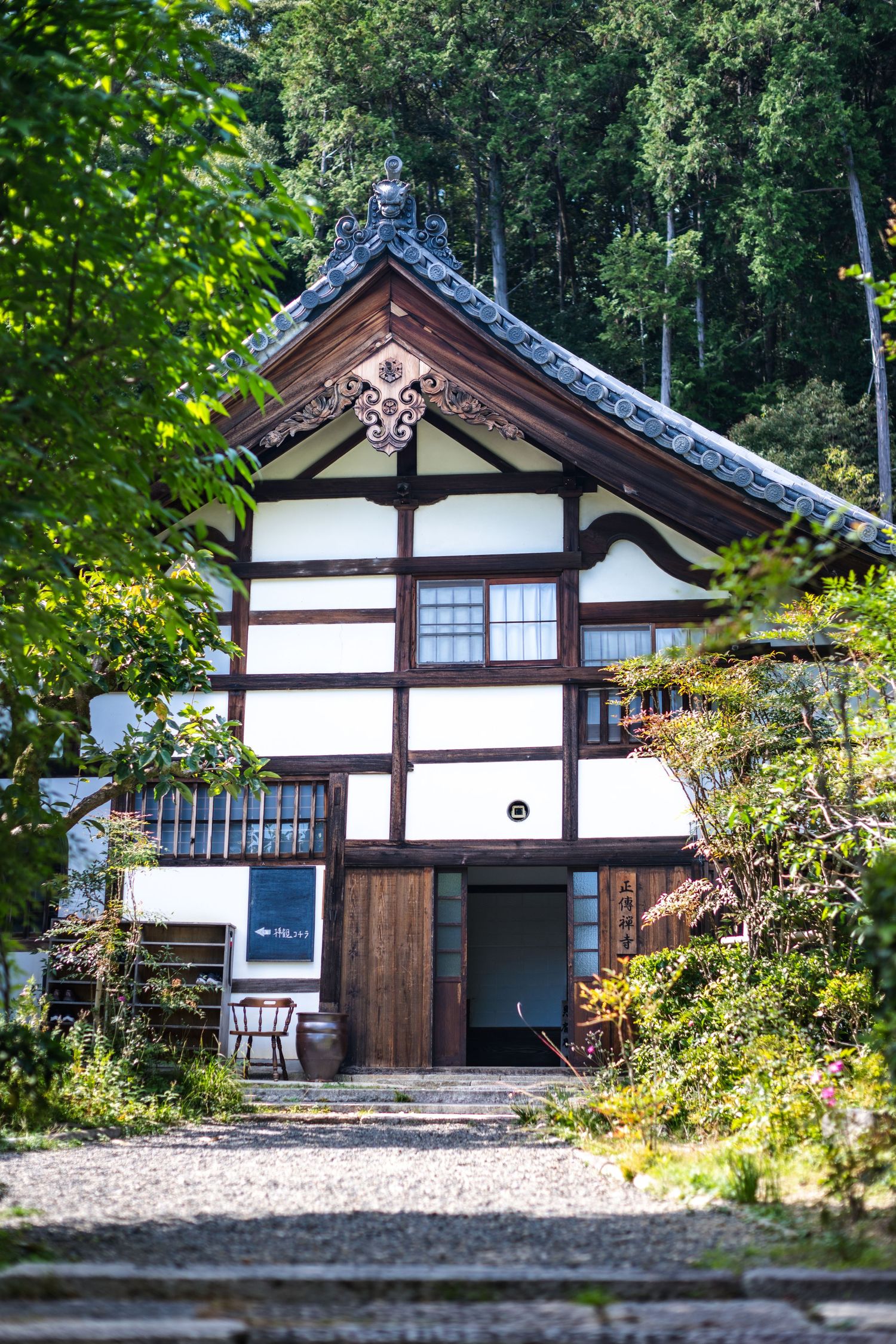 Traditional Japanese wooden temple building with white and dark timber frame nestled among lush green trees.