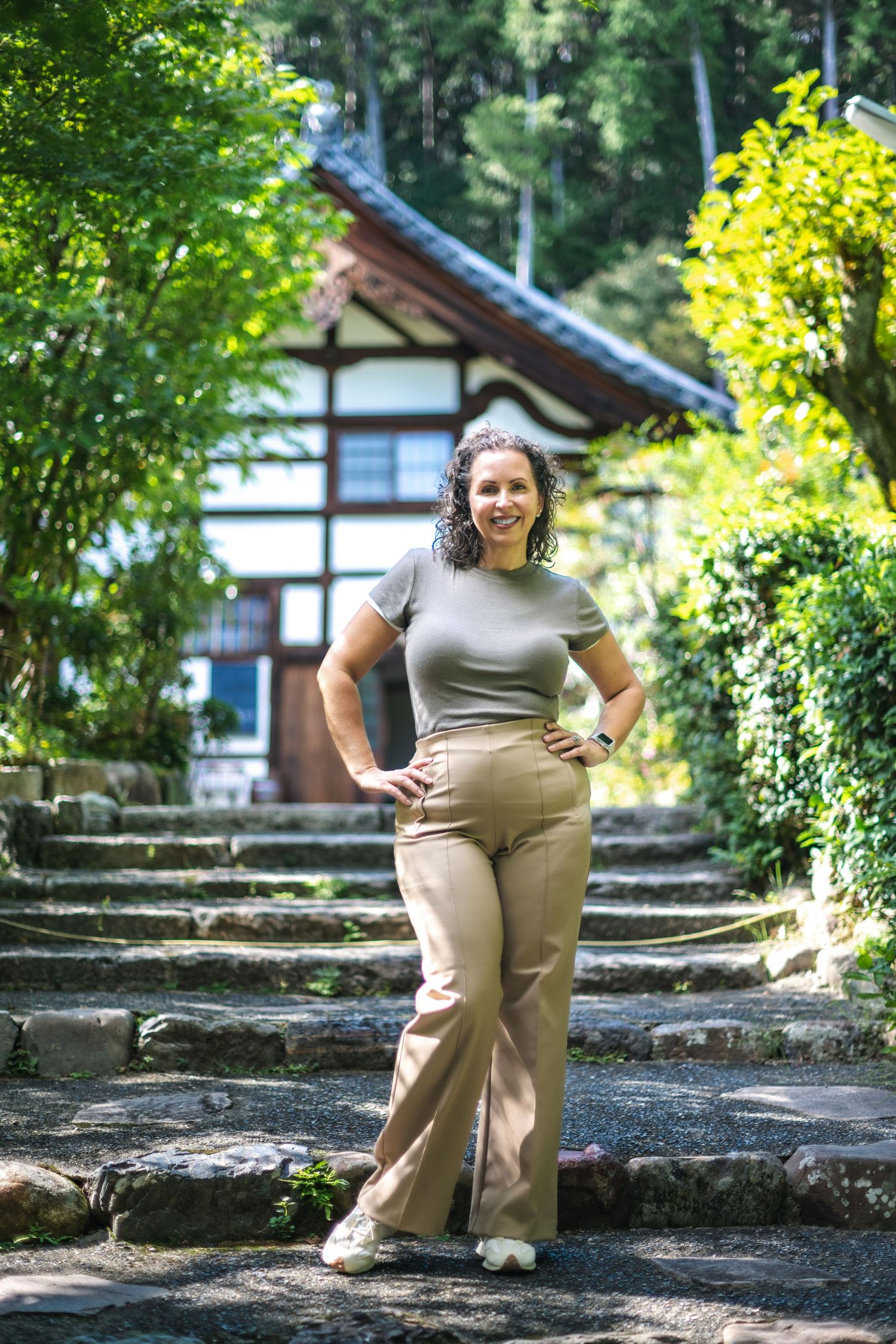 A stone path leads to a traditional Japanese building surrounded by lush green foliage on a sunny day.