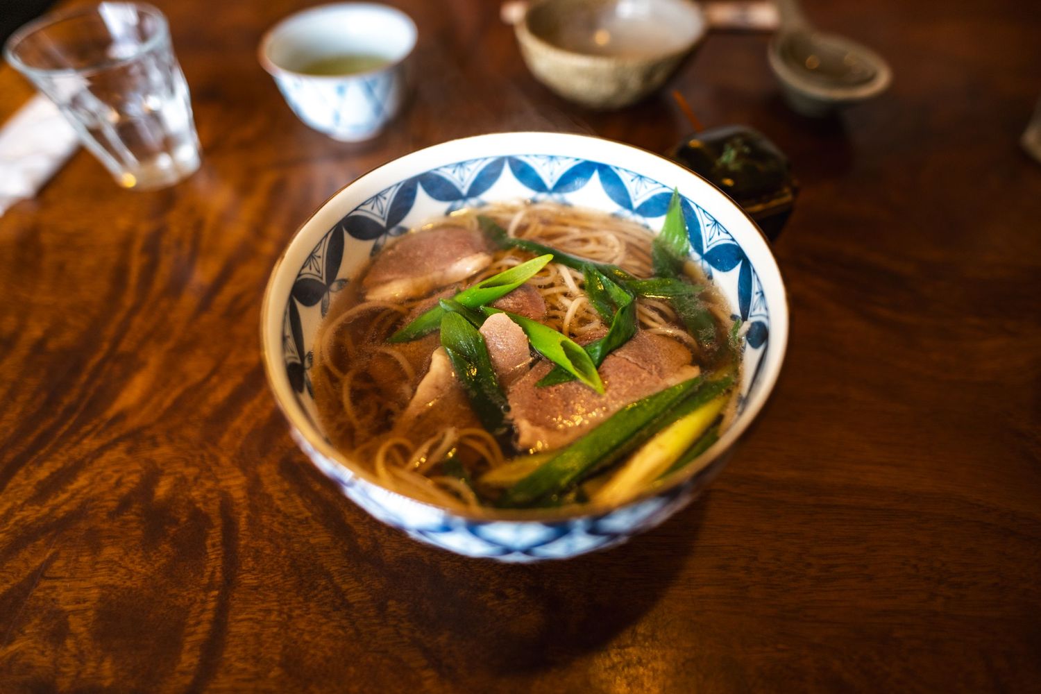 A bowl of Asian noodle soup with meat, green onions and vegetables served in a decorative blue and white ceramic bowl.