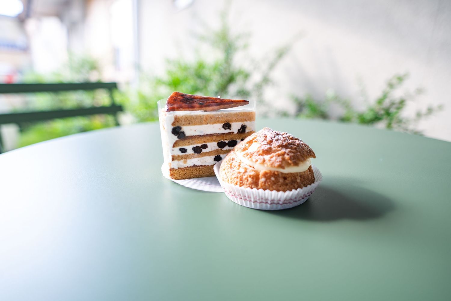 Two delicious-looking pastries sit on a mint green table, including a layered sandwich cookie and a cream puff.