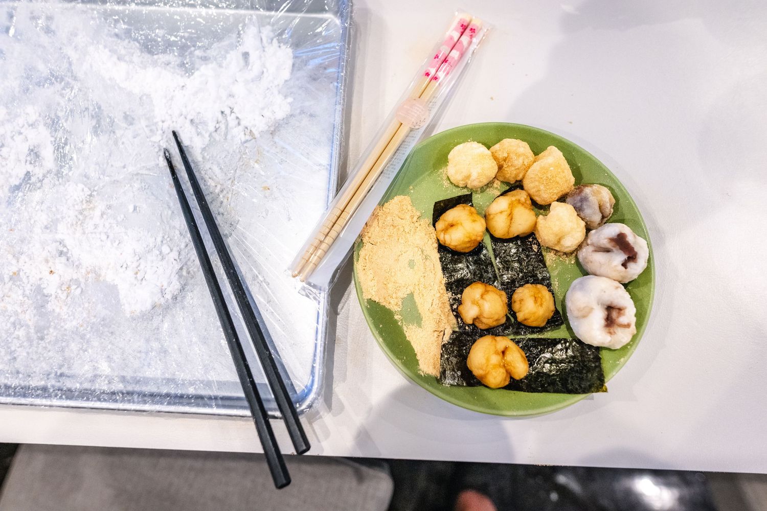 Overhead view of sushi rolls on green plate with chopsticks and sushi mat on light background.