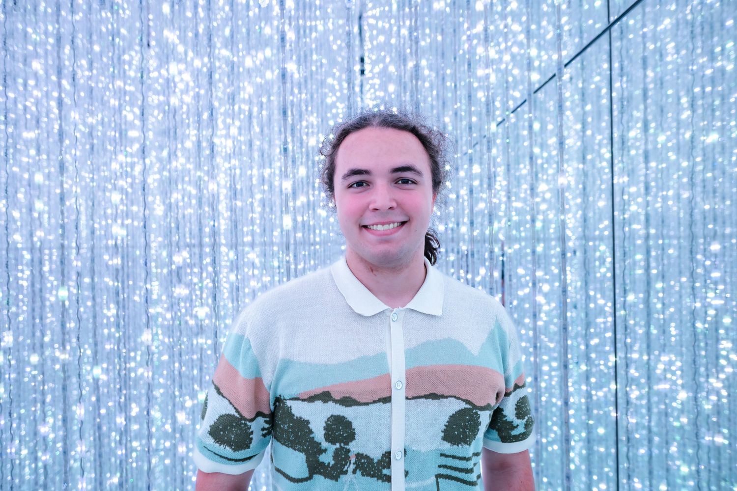 Someone wearing a white and mint green polo shirt stands against a shimmering silver backdrop.