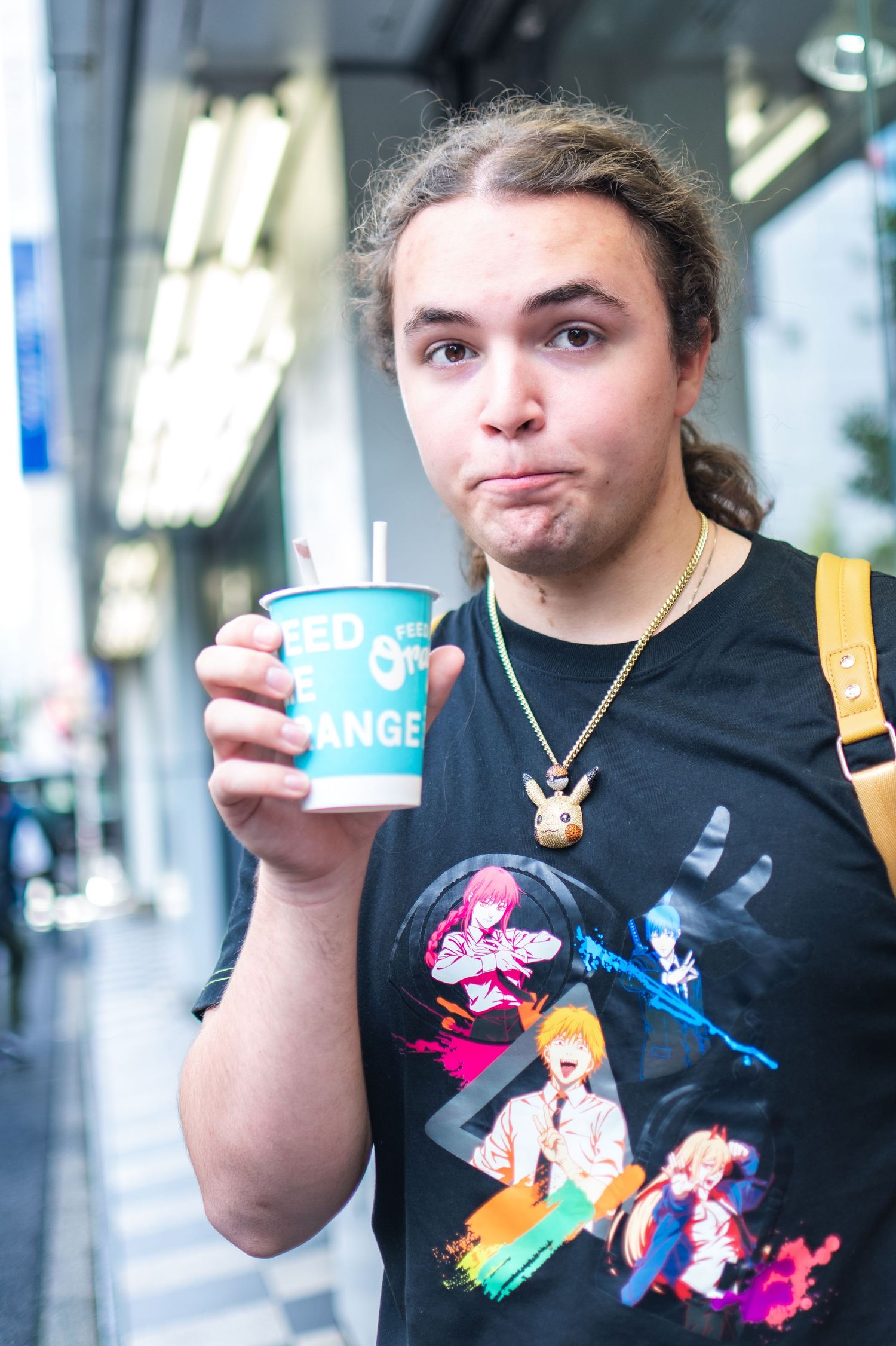 Person in black graphic t-shirt holds a blue takeout cup while standing in front of fluorescent lights.
