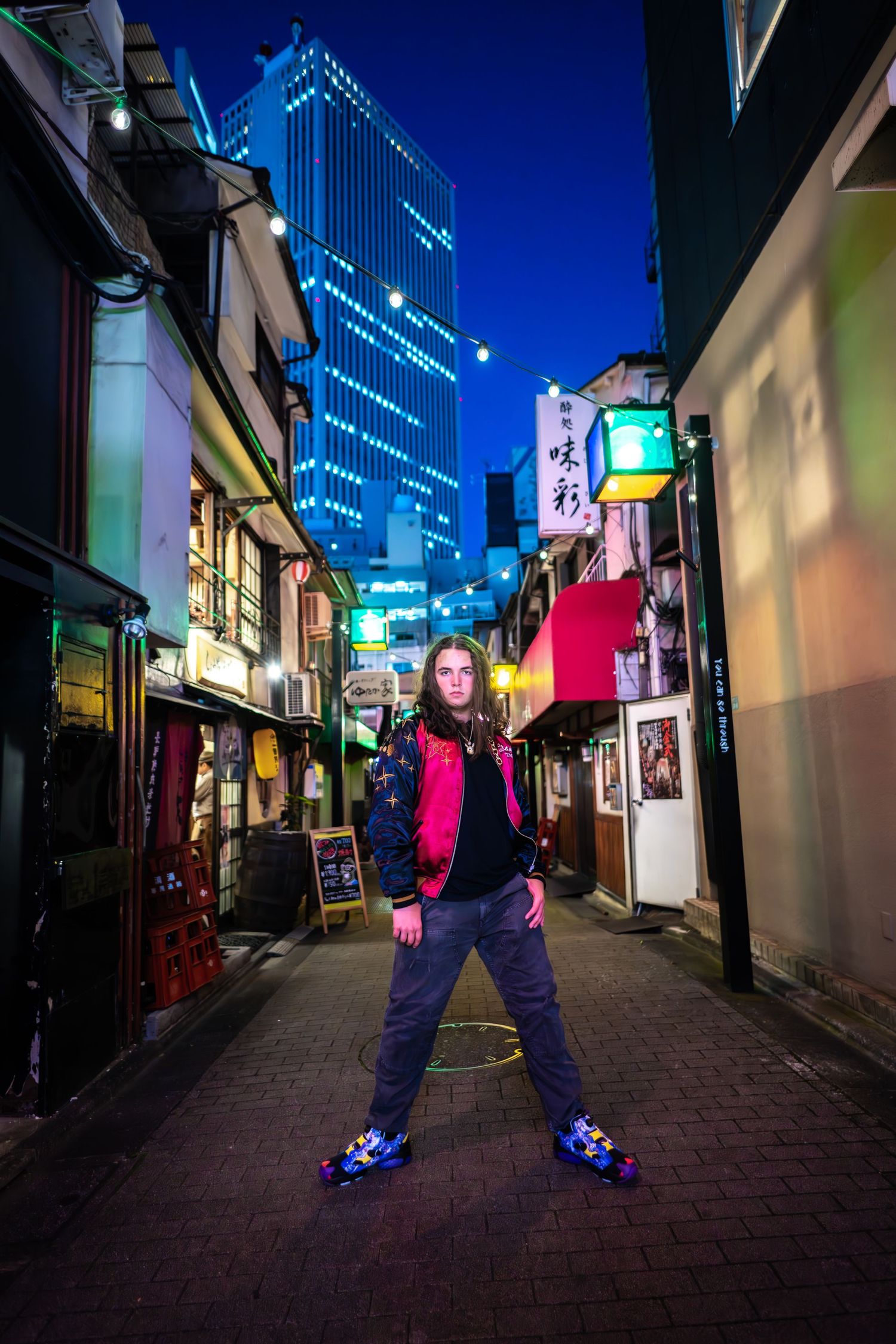 Vibrant nighttime street scene in Tokyo with neon signs and tall skyscraper glowing blue against dark sky.