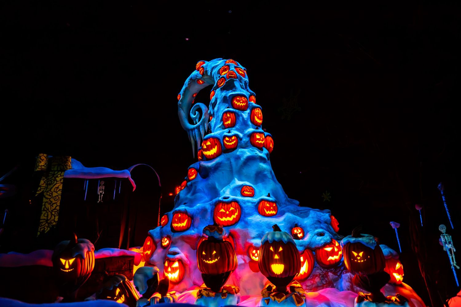 Illuminated Halloween pumpkin display glowing with blue and orange lights in a spooky nighttime scene.