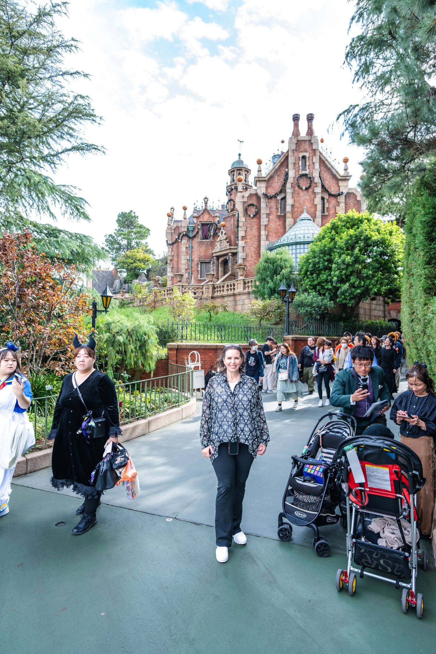 Visitors walking along path near Haunted Mansion attraction at Disney theme park with Gothic architecture in background.