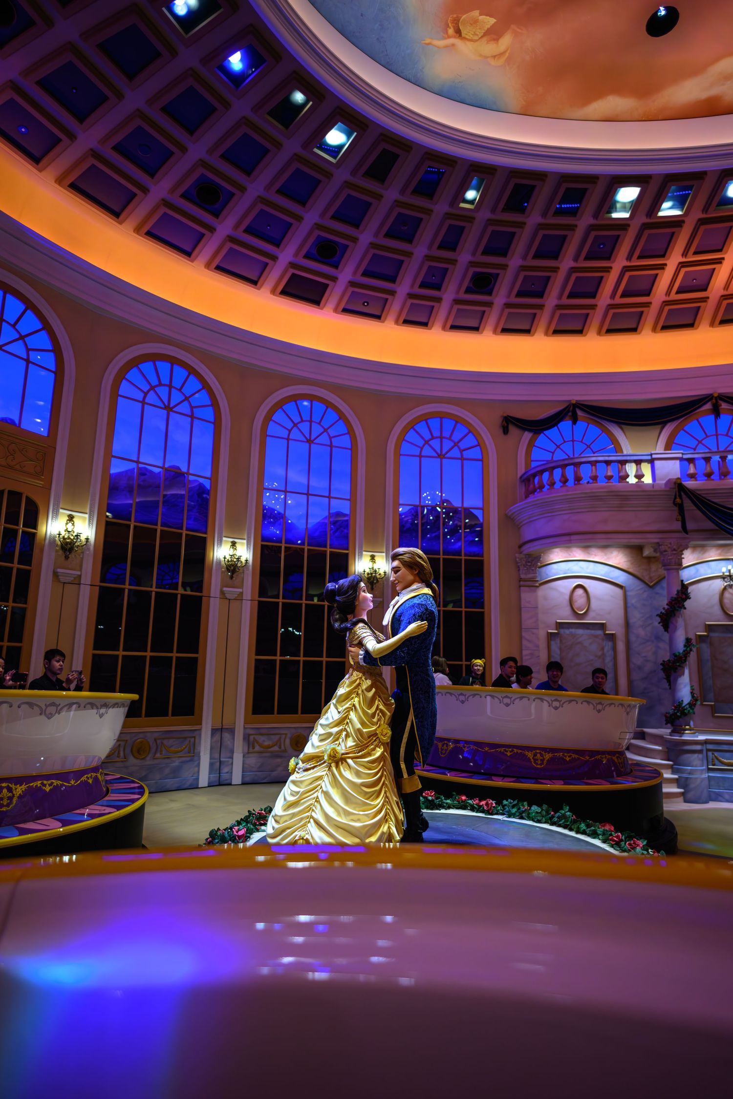 Interior of elegant ballroom with domed ceiling and arched windows illuminated in blue and gold lighting.
