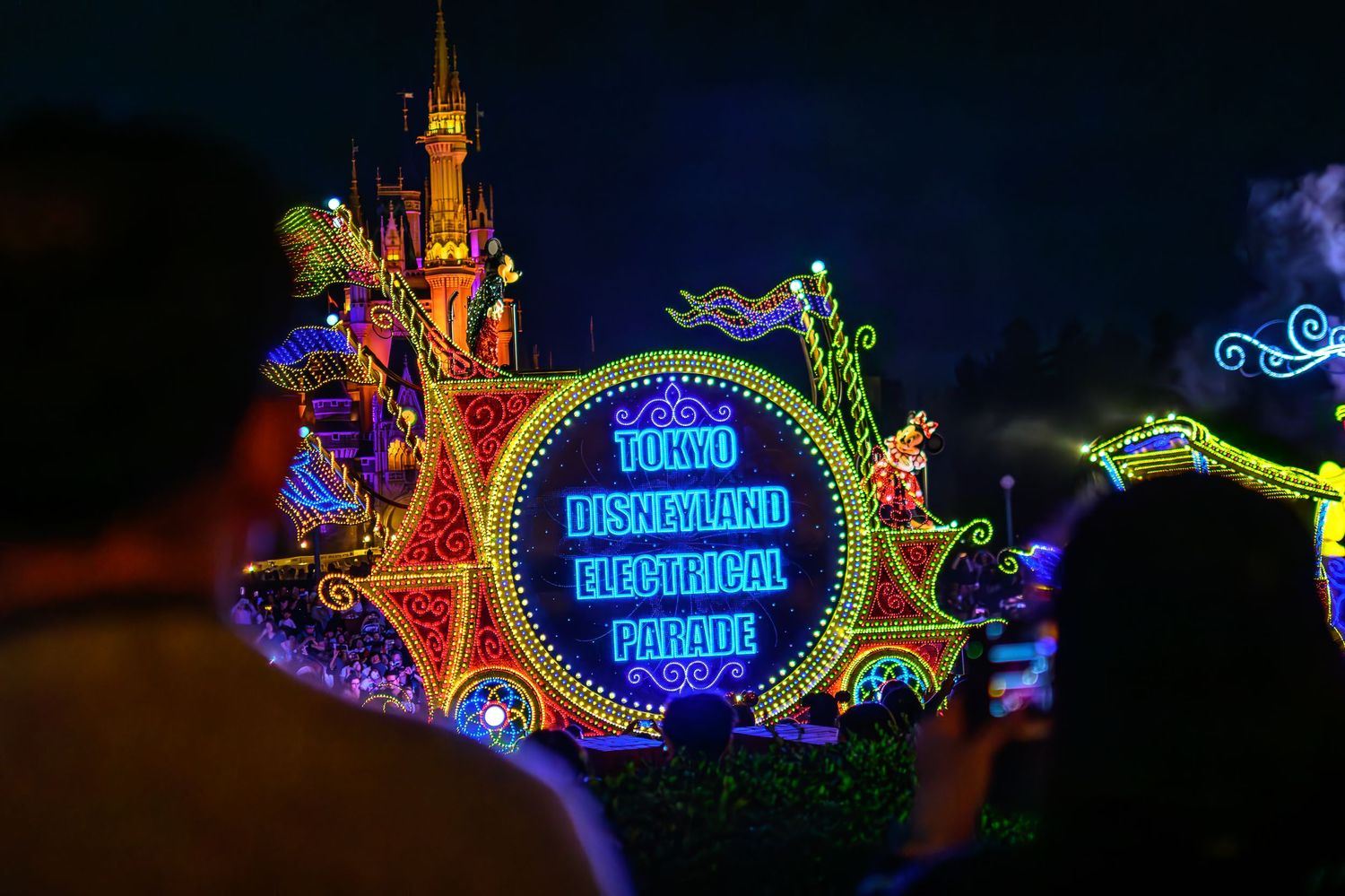 Colorful illuminated Main Street Electrical Parade float with neon lights and castle silhouette at night.