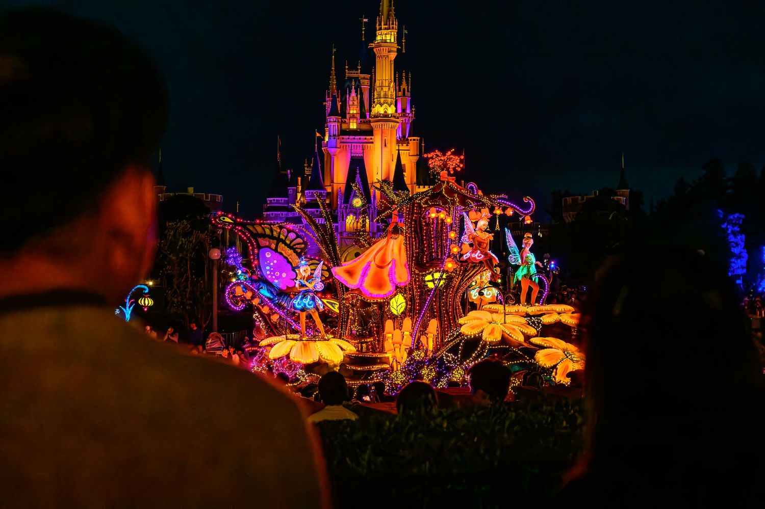 Illuminated Disney castle at night with colorful projections and crowd silhouettes during a nighttime show.