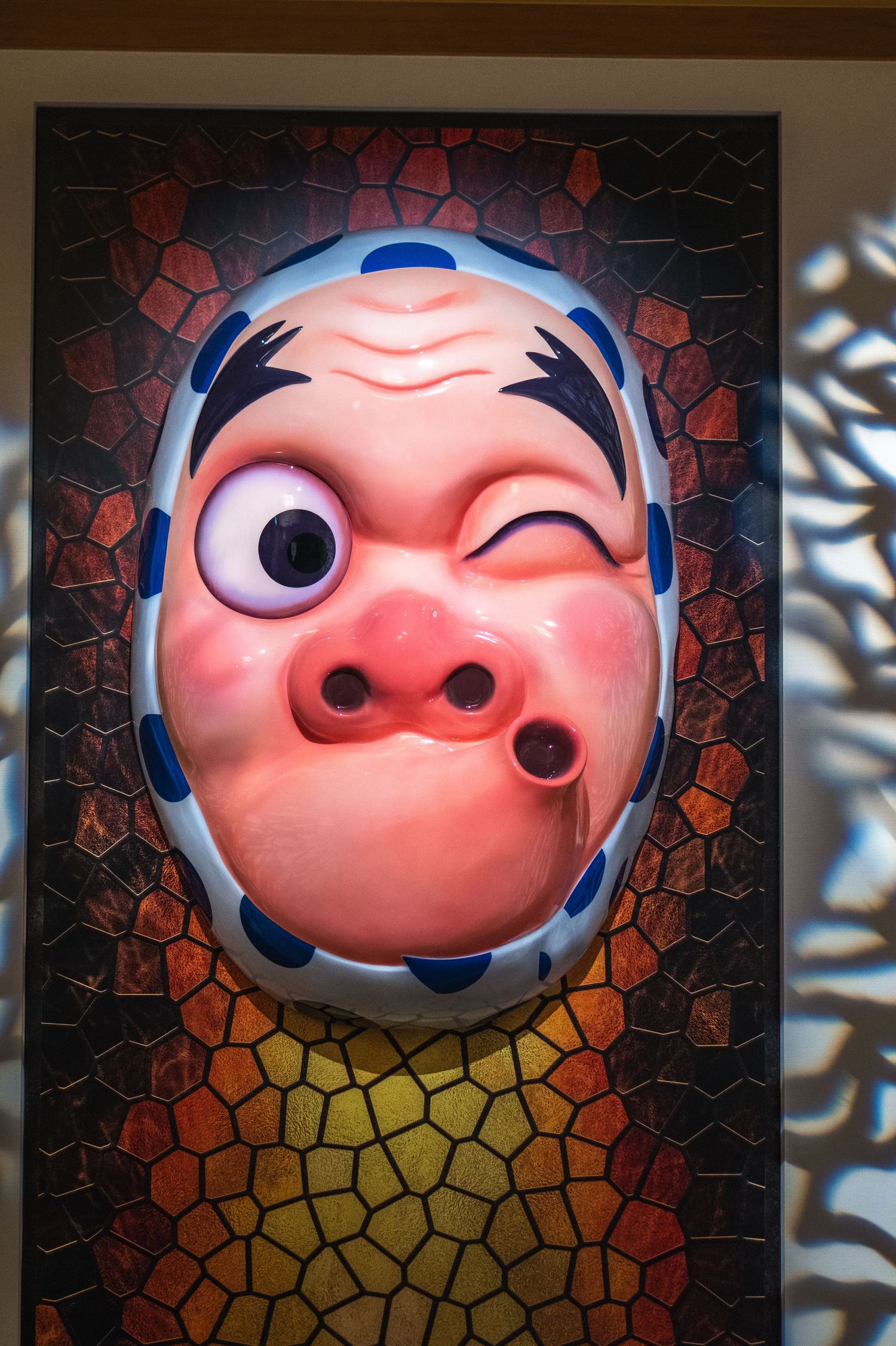 Pink Japanese pig mask with wide eyes and winking expression displayed against mosaic tile background.