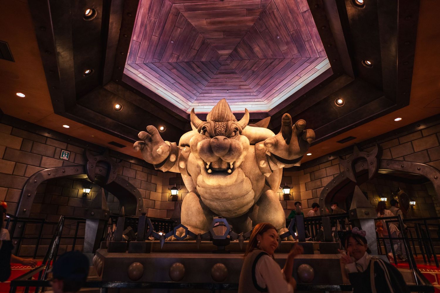 A large animatronic Bowser statue looms menacingly inside a Nintendo-themed attraction with dramatic purple lighting.