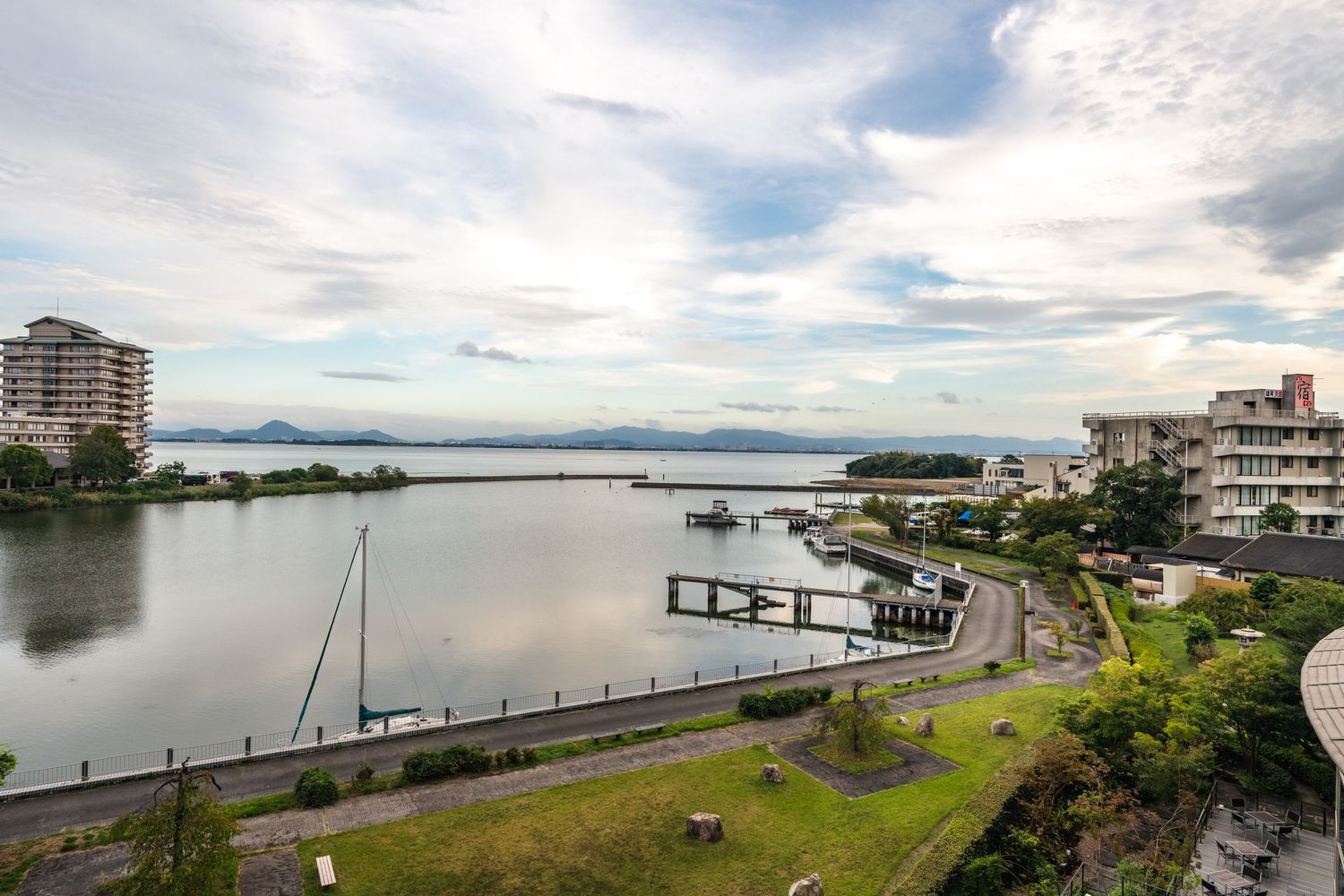 Scenic waterfront view of Lake Rotorua with boats moored at the pier and mountains in the distance under cloudy skies.