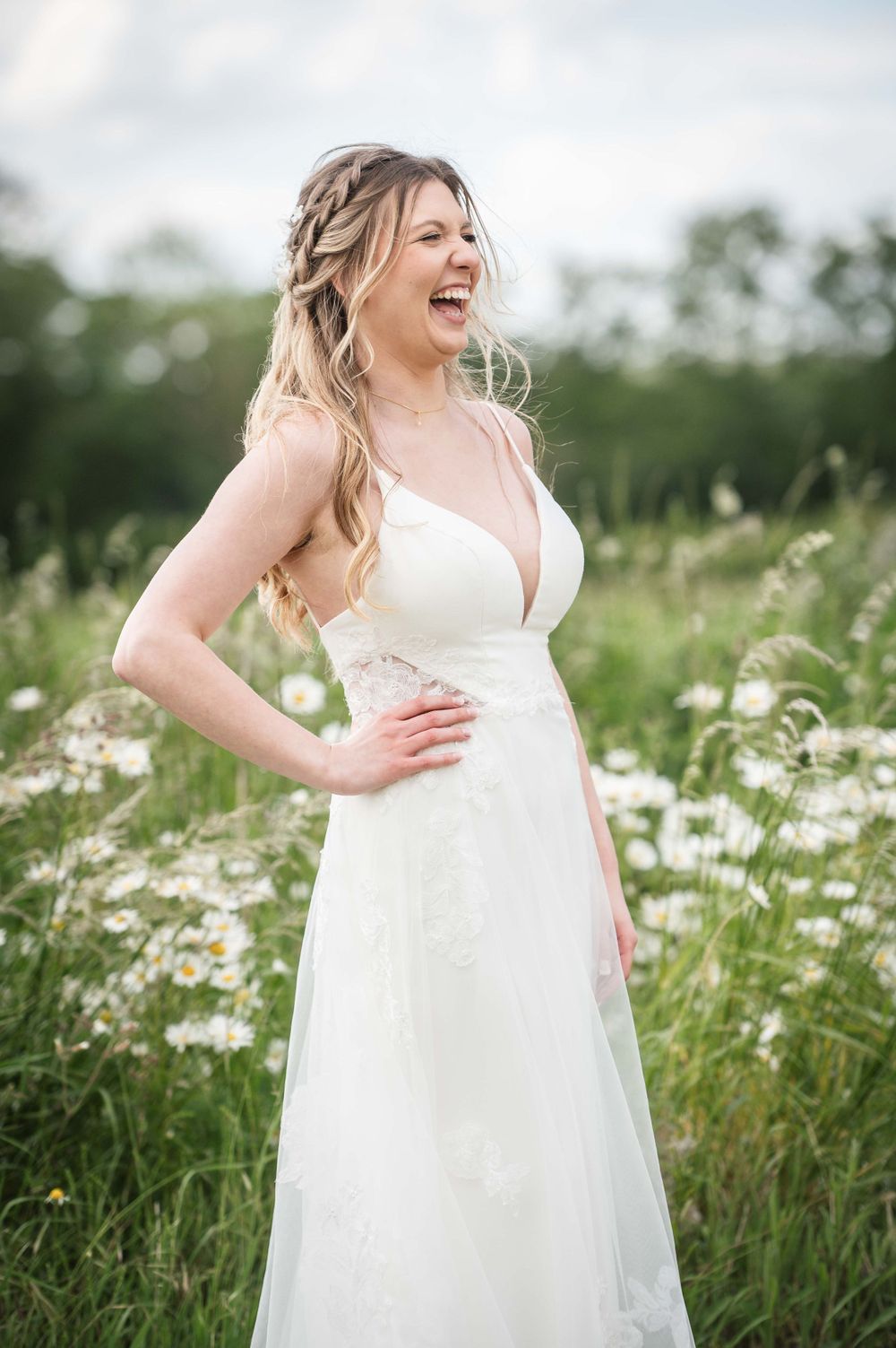A joyful bride in a white flowing dress laughs while standing in a wildflower meadow on a summer evening.