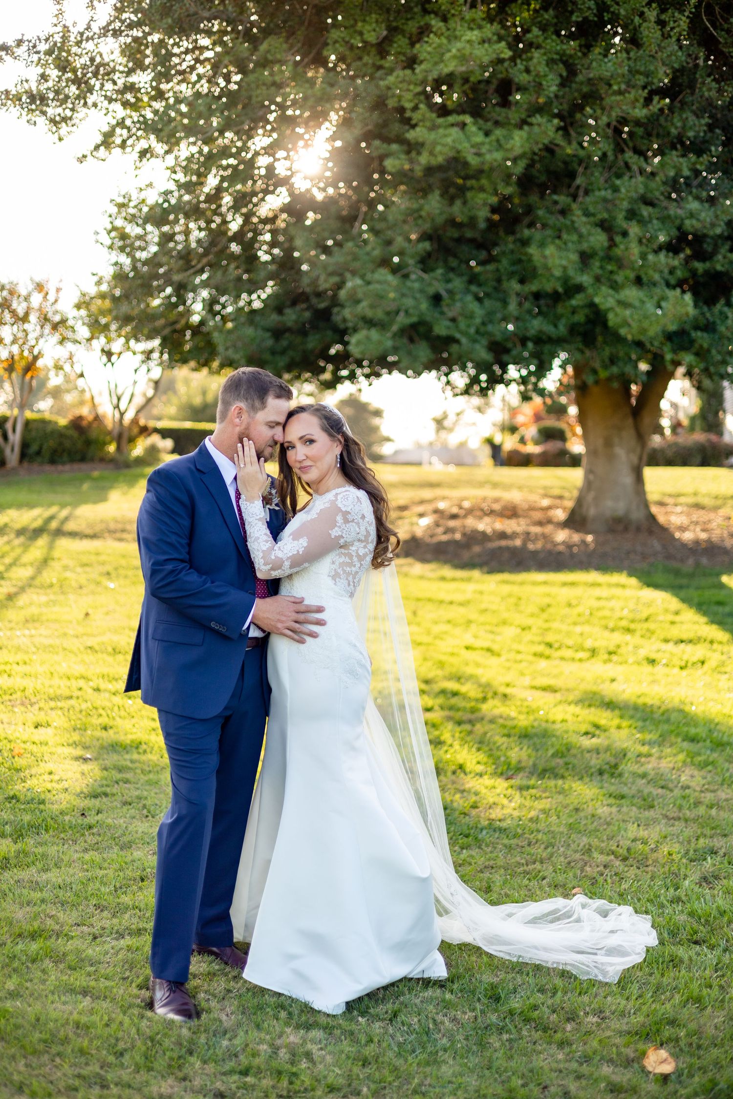 Wedding couple embracing in sunlit garden with flowing white dress and veil.