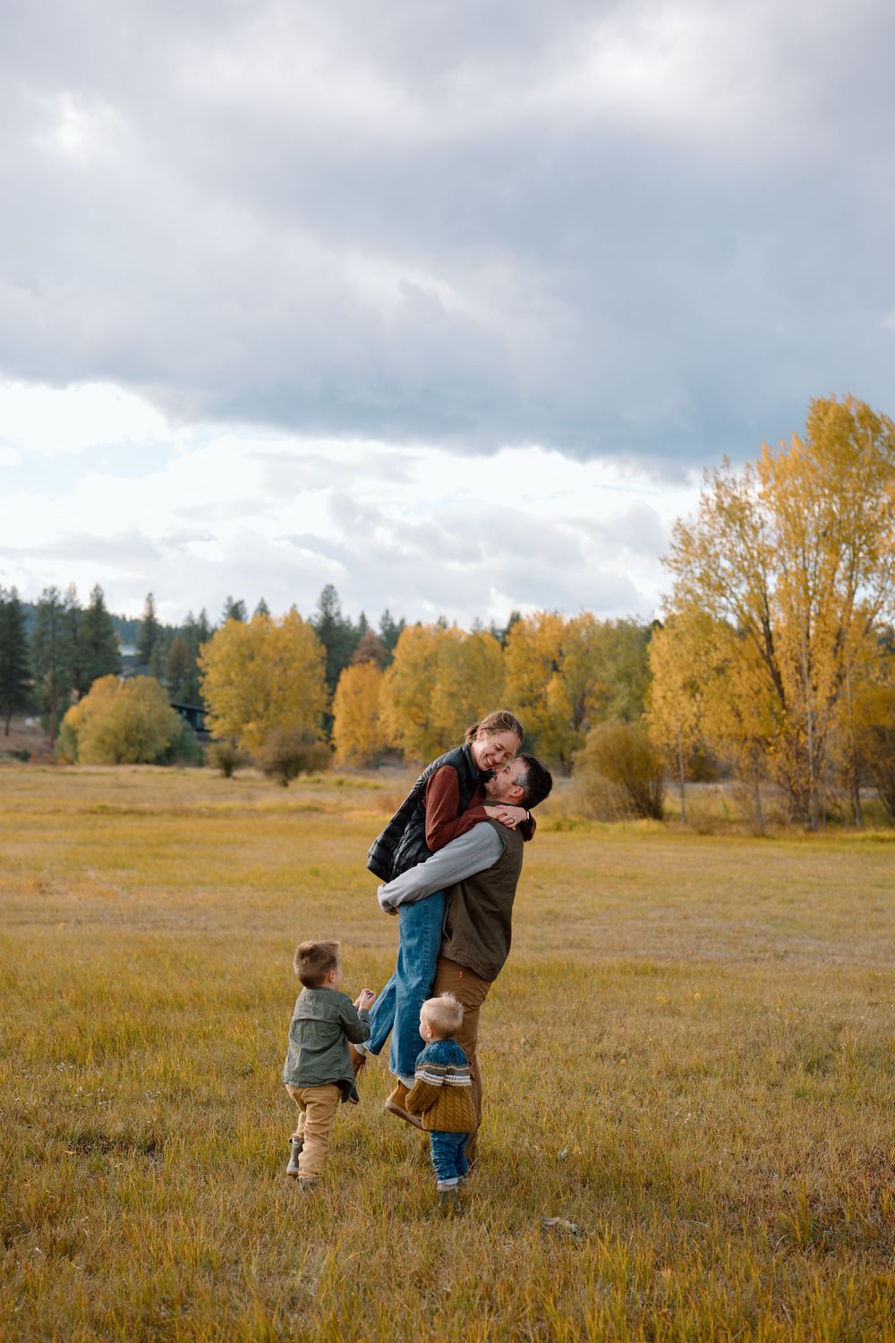 People walking together through a golden autumn meadow with tall trees and cloudy skies in the background.