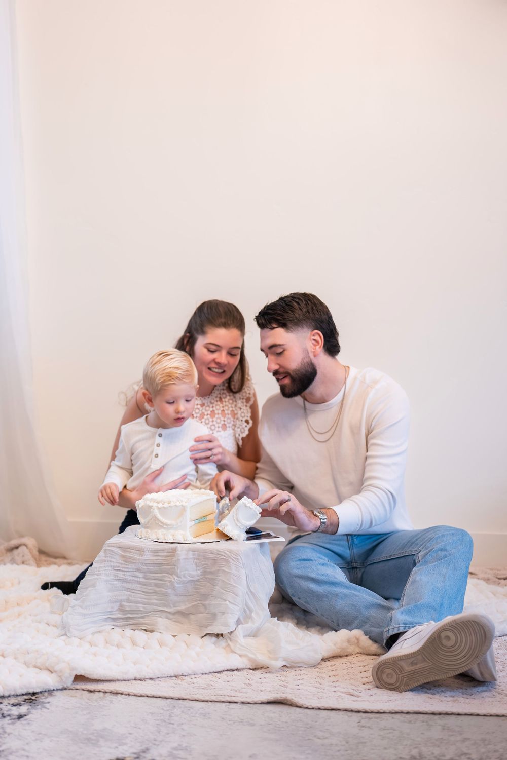Family sits together on floor sharing cake while celebrating a special occasion at home.
