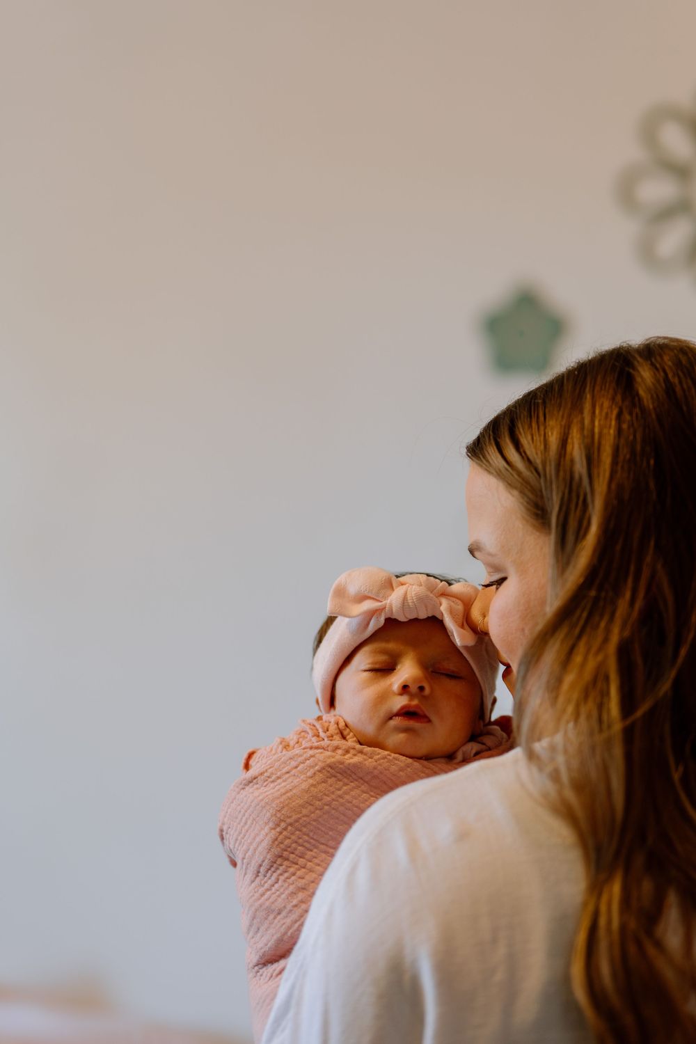 A parent holds and comforts a crying baby in a soft pink sweater against a light background.