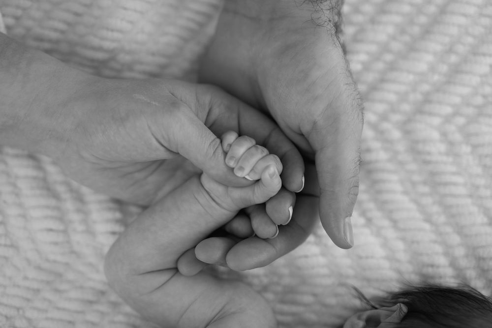A tender black and white image of adult hands gently holding a tiny baby's foot against a soft textured background.