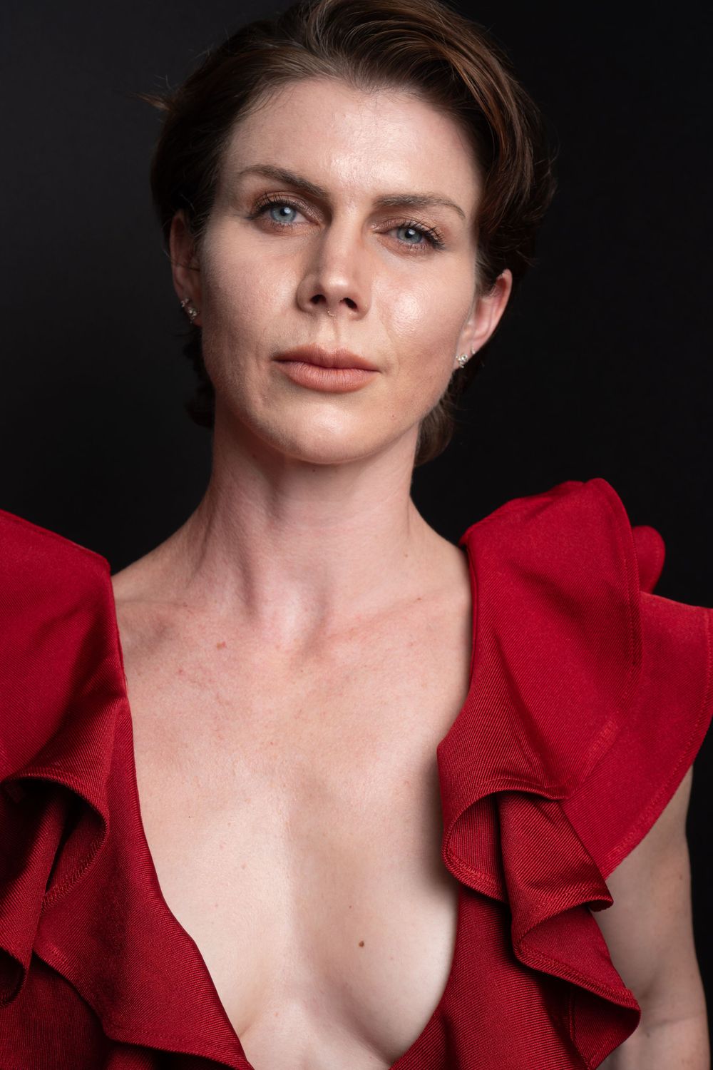 Close-up fashion portrait featuring dramatic red ruffled top against dark background.