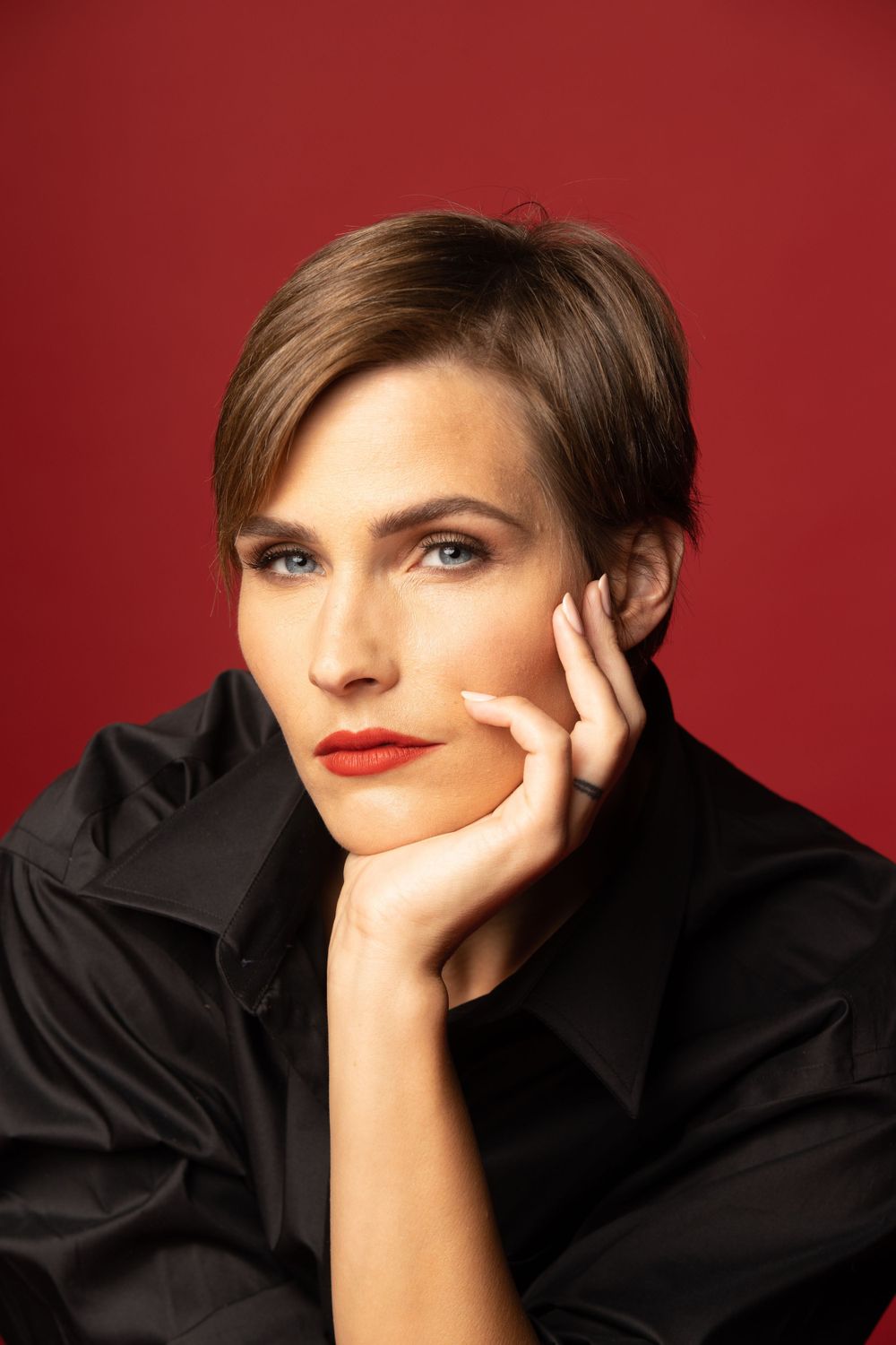 Classic studio portrait against red background wearing black shirt, red lip stick.