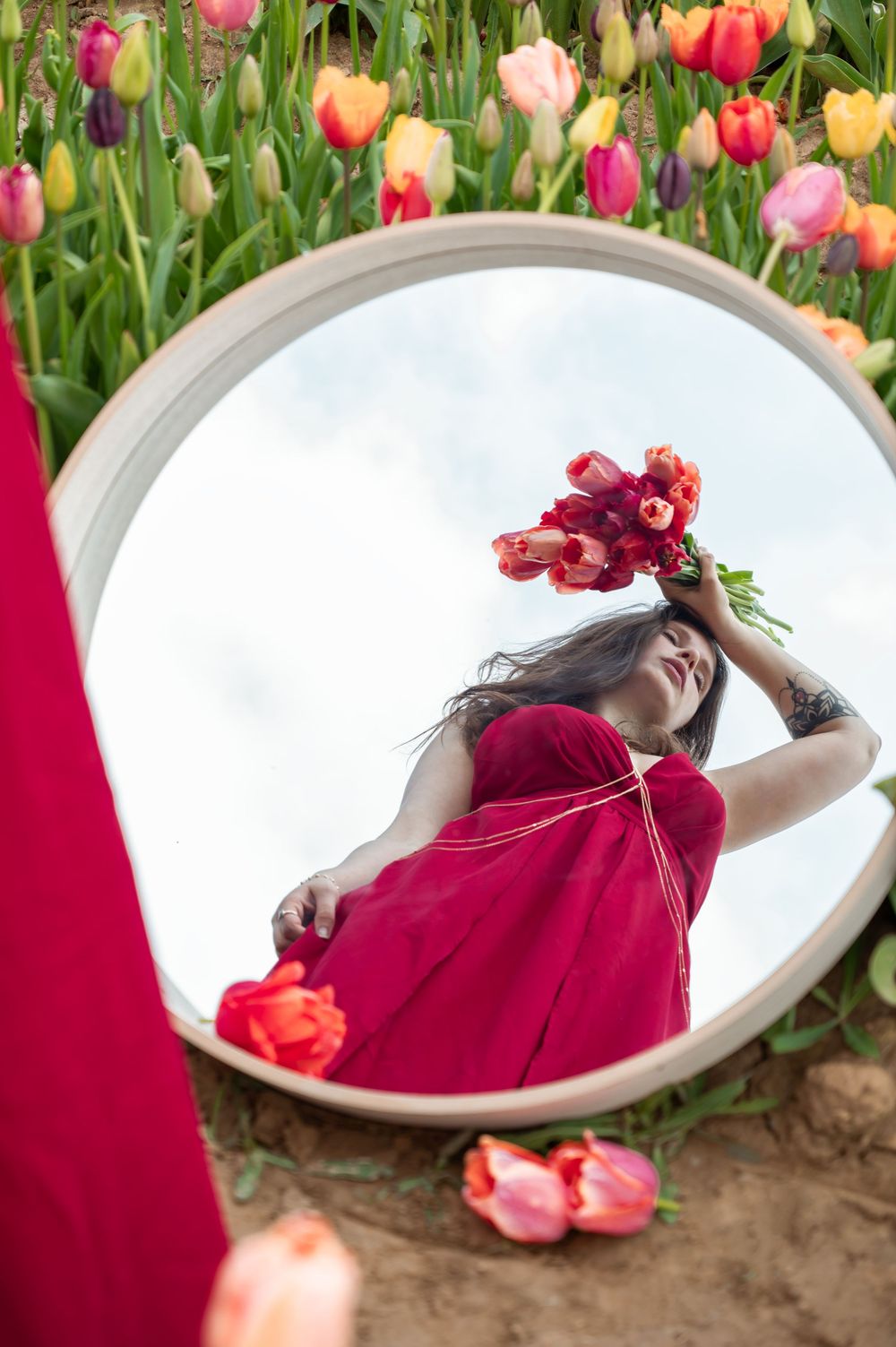 À Namur, portrait individuel d’une femme photographiée dans un champ de tulipes avec un miroir et un bouquet de fleurs