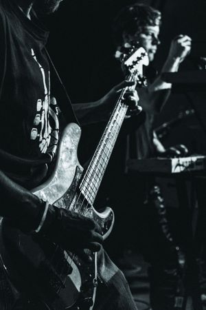 Black and white shot of a musician playing bass guitar on stage during a rock performance with dramatic lighting.