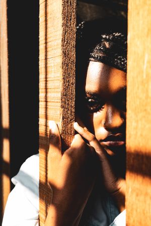 Artistic portrait through wooden slats with warm sunlight creating dramatic shadows.