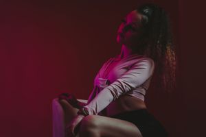 Dramatic fashion portrait with red lighting and white crop top in studio setting.