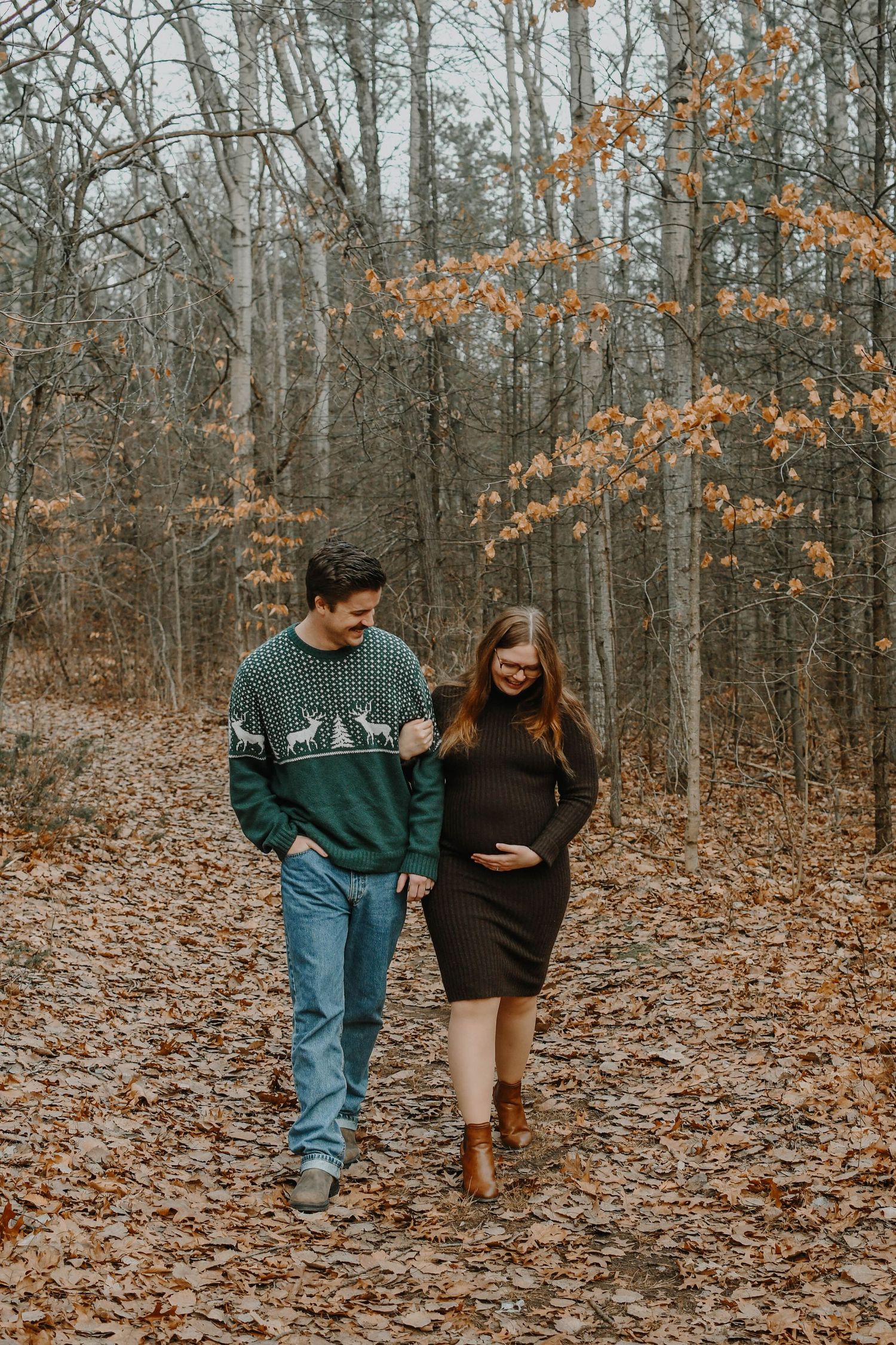 A couple walks together on a leaf-covered forest path during autumn while enjoying a tender moment.