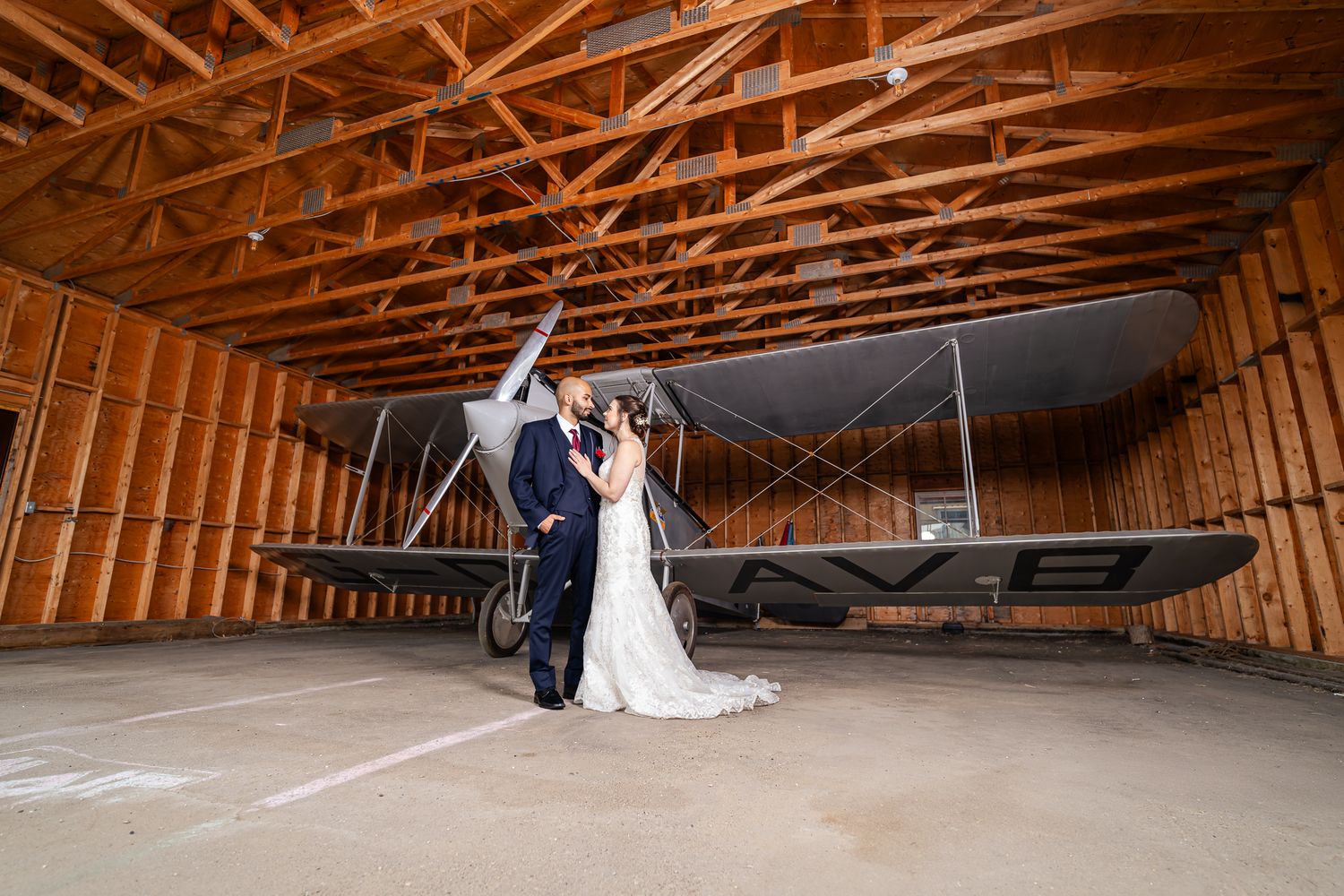 A couple shares a romantic moment in a rustic barn venue with exposed wooden beams and soft lighting.