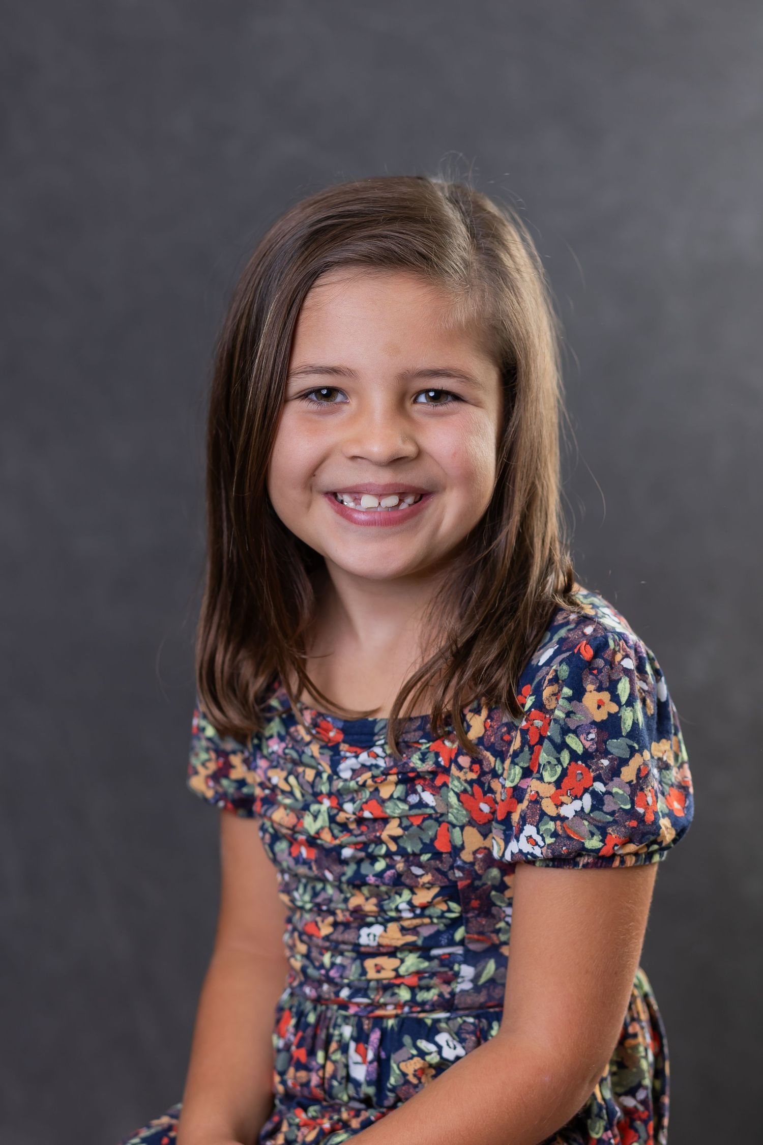 Studio portrait of a child wearing a colorful floral print dress against a gray background.